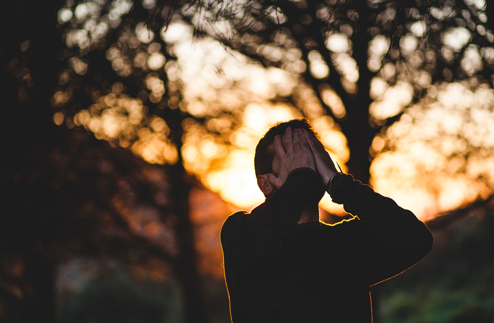 A young person places his hands on his face, with trees in the distance.