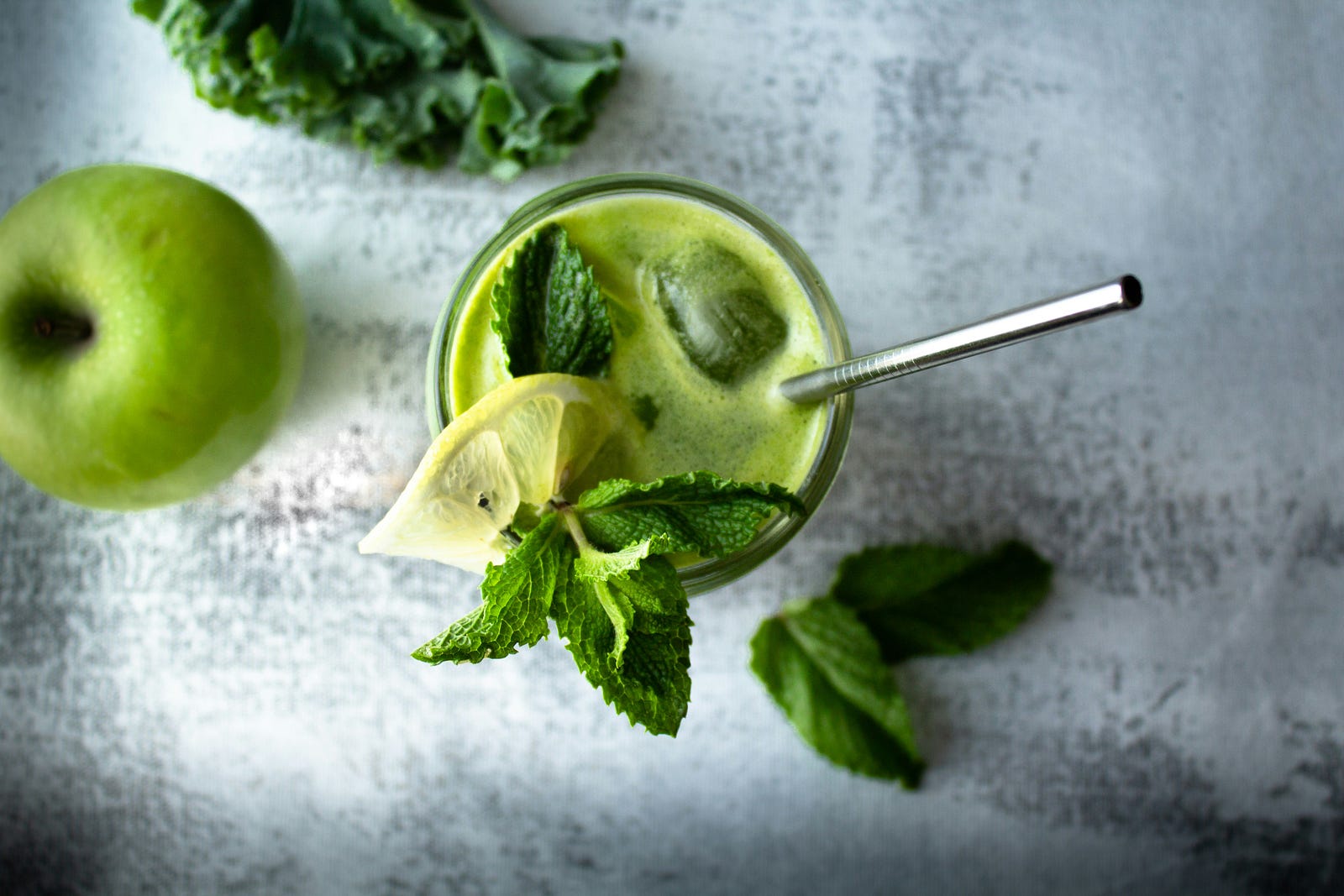 Green juice, in a glass with a silver spoon and leaves in it.