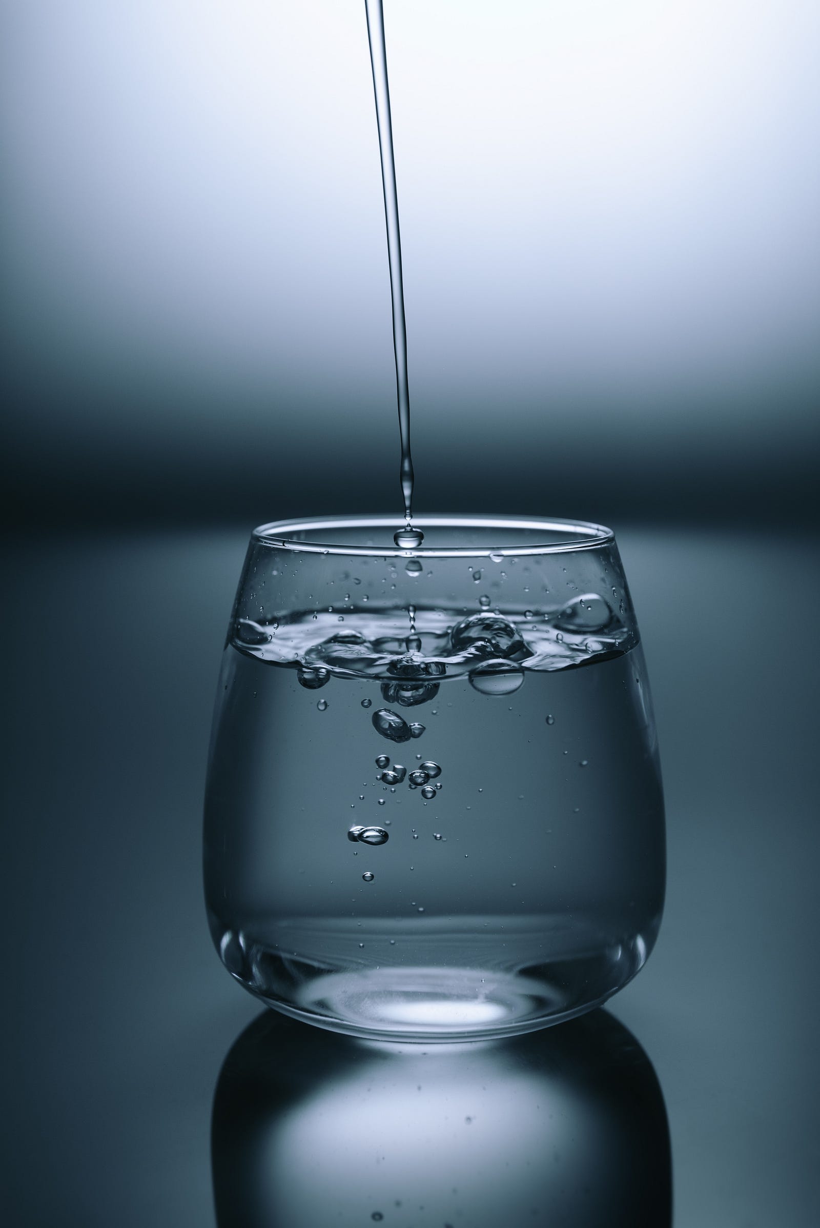 A stream of water pours from above into a nearly full drinking glass. Water is not only essential for overall well-being but can also aid in digestion and prevent overindulgence. If I consume any alcohol, I make it a point to alternate alcoholic drinks with water and consider infusing water with seasonal fruits for a refreshing twist.