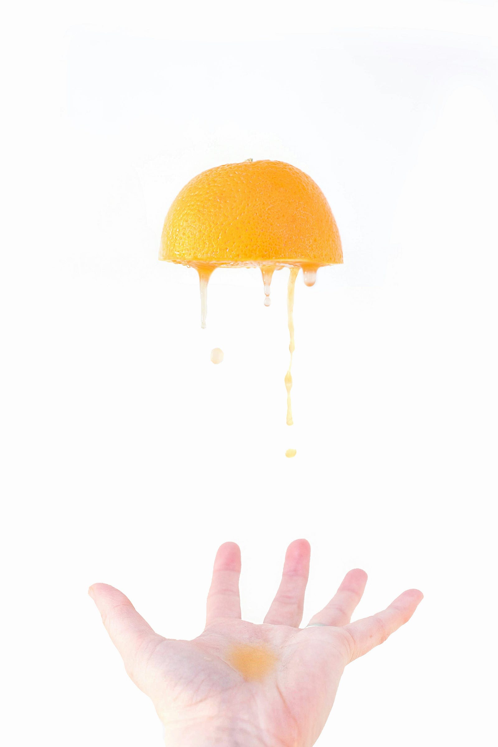 A hand throws a half orange up, with juice spilling from the bottom of the fruit.