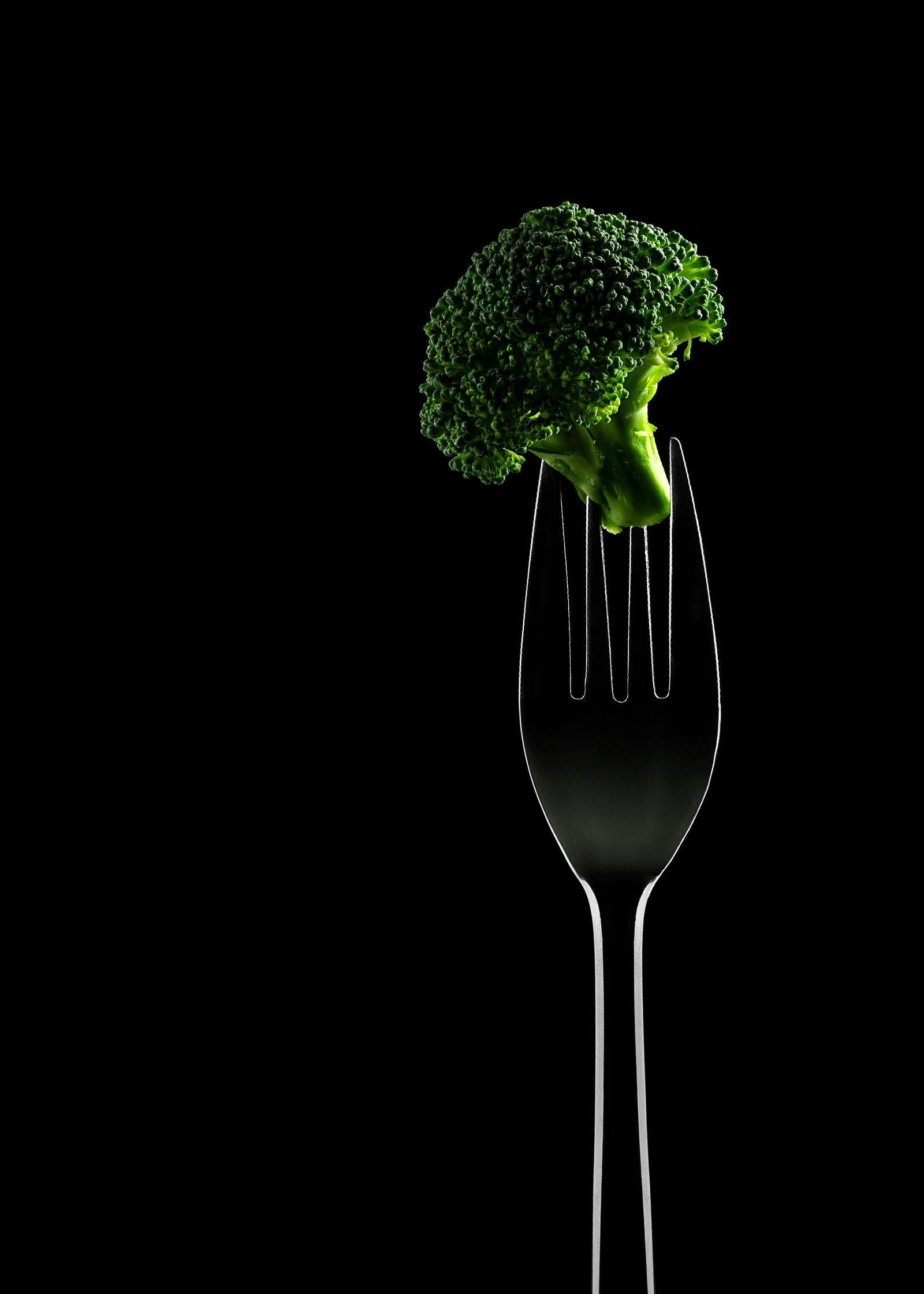 A fork sticks up, with a piece of brocolli on its tines.