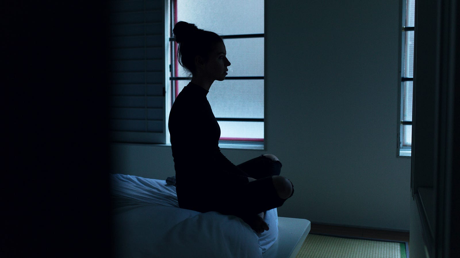 A woman, seen in profile, sits in a cross-legged pose on the end of her bed. A well-rested immune system is a formidable one.