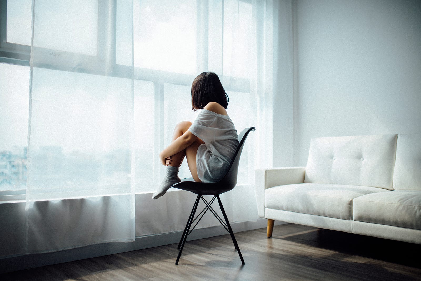 A young brunette woman gazes out of the window of a light filled room. She is curled up in a chair, knees up to her chest. If rTMS (repetitiive trascranial magnetic stimulation) is effective for you, depression symptoms may improve (or resolve). Symptom relief may take a few weeks of treatment.