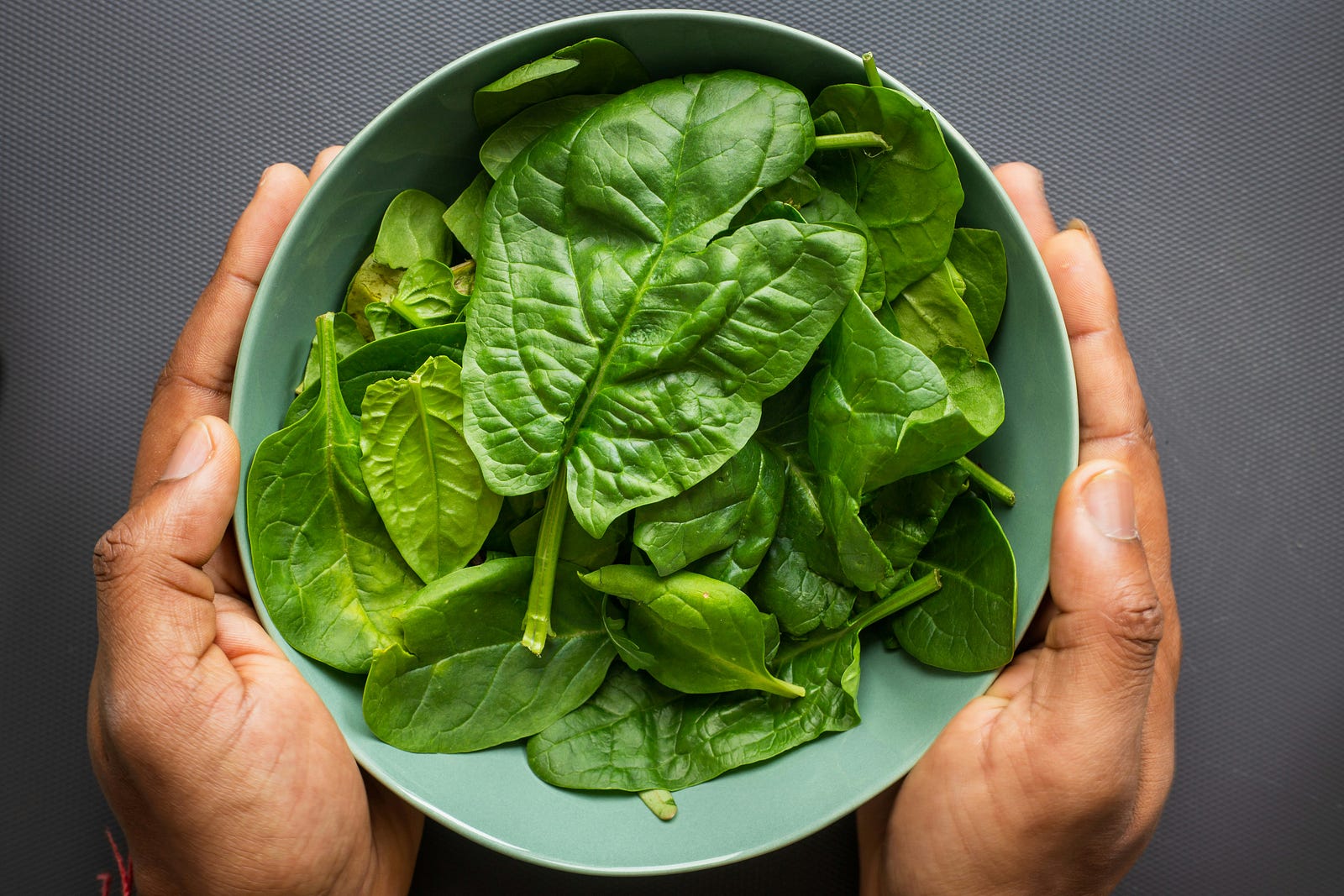 A person holds a round blue plate of spinach. The vegetable is rich in vitamin B12.