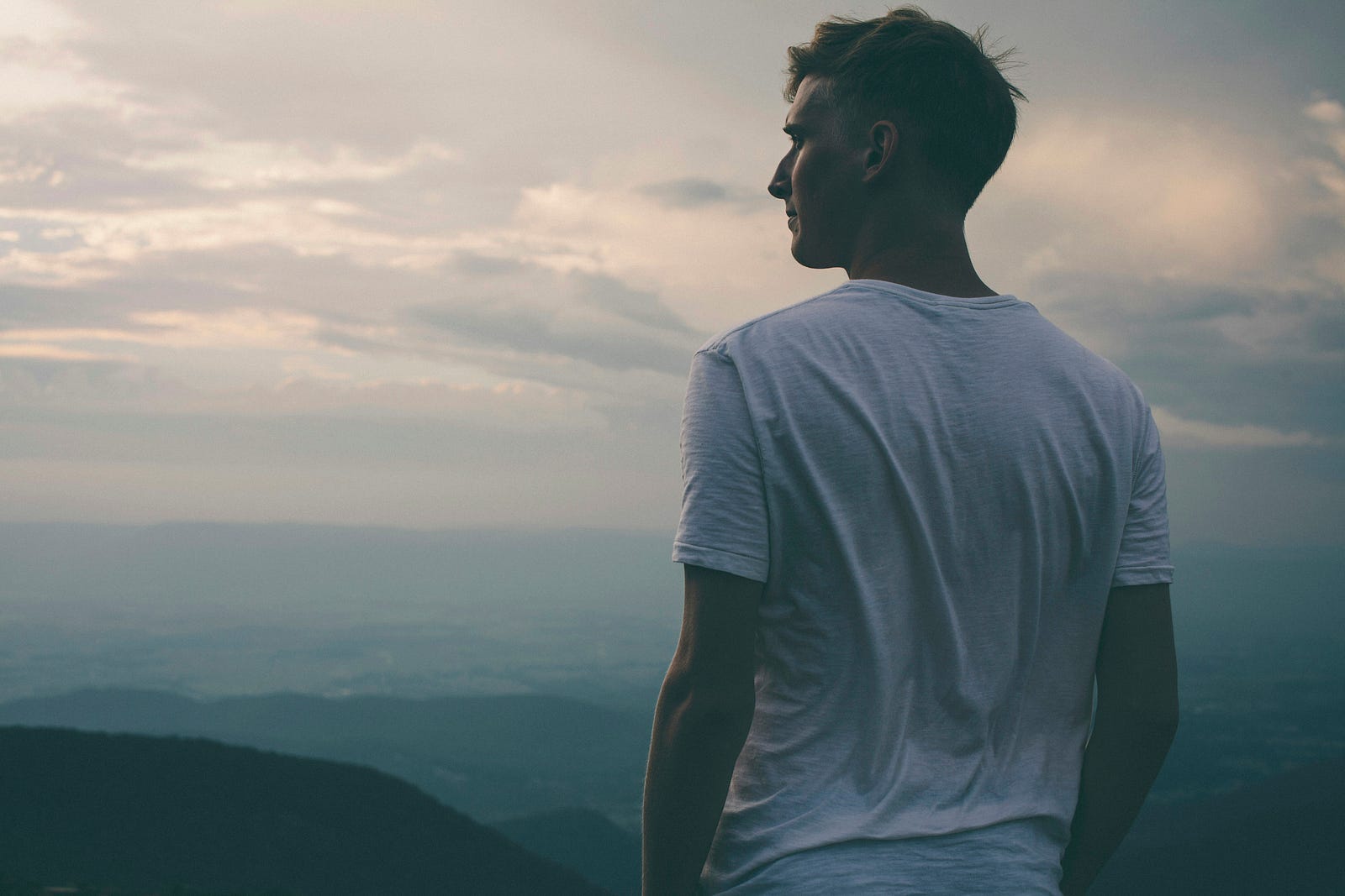 A young man in a T-shirt gazes into the distance (mountains).