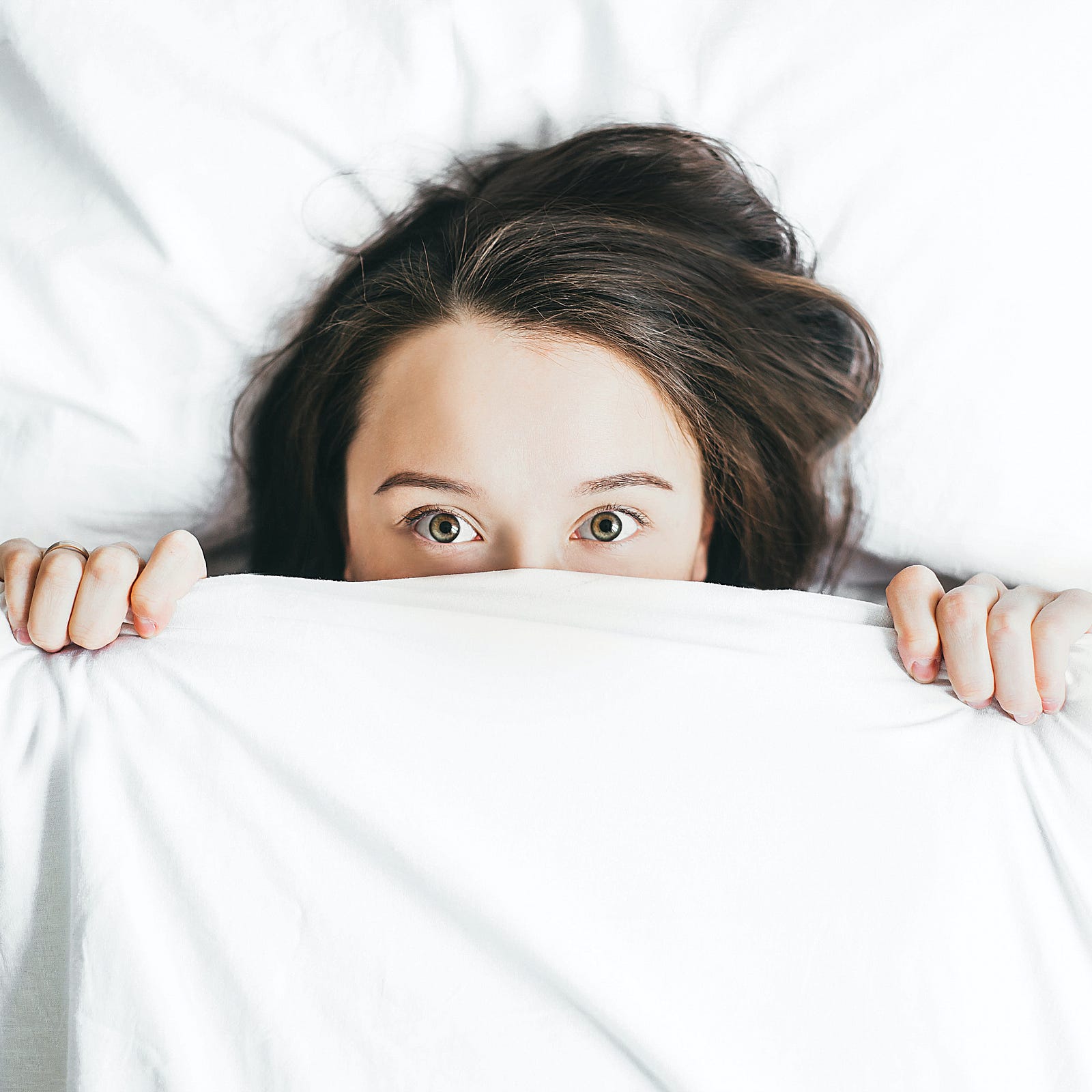 A woman lies on her back in bed. She peers out over her sheets; we see her from mid-nose up. About 5 percent of women go into early menopause, having symptoms between ages 40 and 45. One percent go into premature menopause before reaching age 40.