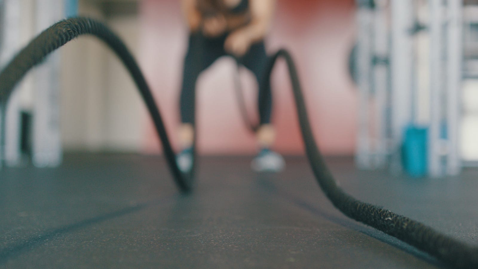 A blurred person in the distance works with black ropes, one in each hand. HIIT has emerged as a scientifically supported method to enhance fitness levels and promote weight loss efficiently.