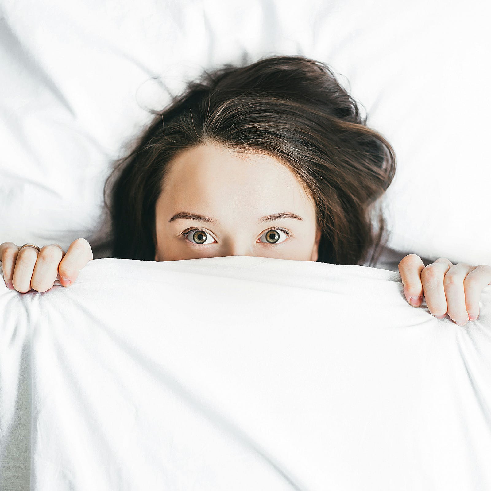 A woman looks up at us as she pulls a white sheet to cover the bottom part of her face.