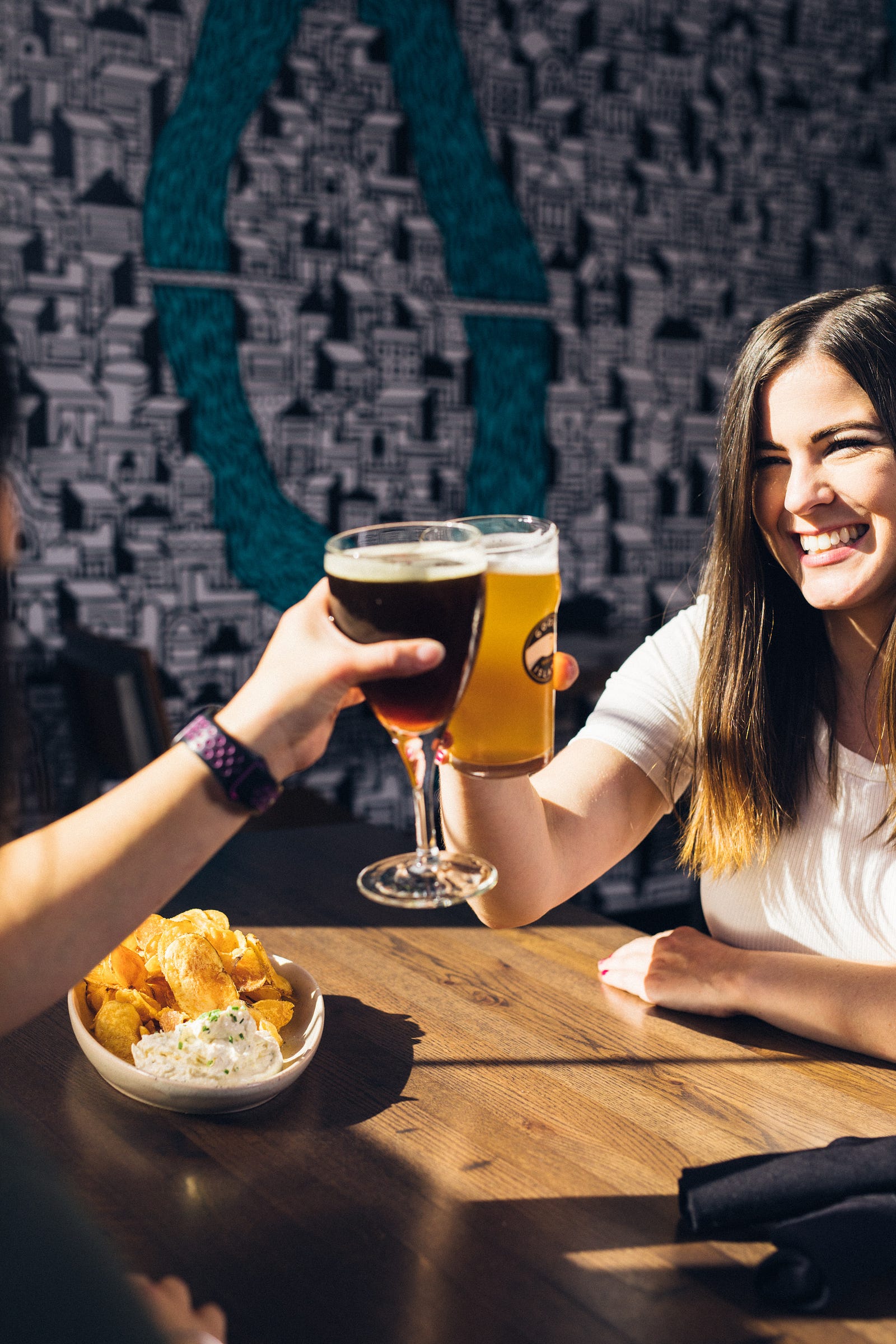 A couple clicks their glasses of beer together. We see the smiling woman on the left and an extended left arm of someone out of image on the left. Approximately 3.5 percent of cancer deaths in the United States (and four percent worldwide) per year are related to alcohol.