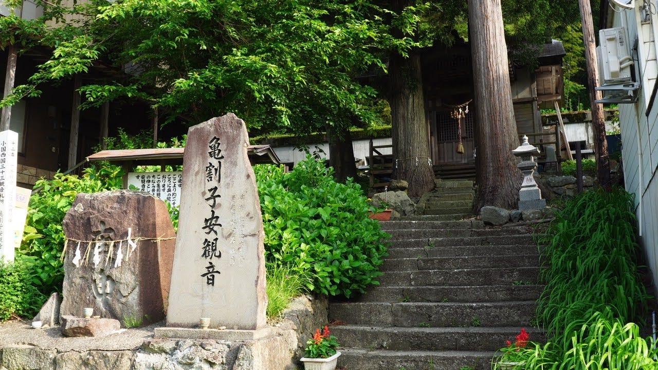 Kamewari Koyasu Kan’on shrine with huge trees in front of it, and then stone monuments in the foreground.