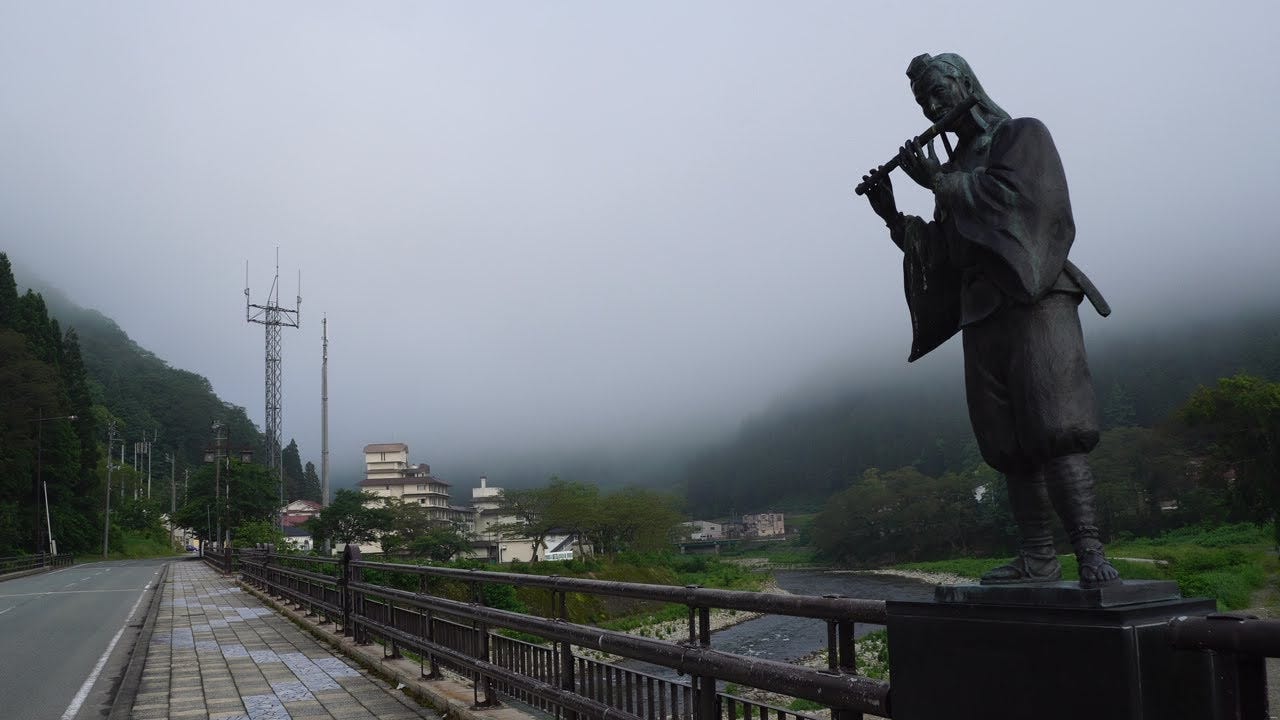 A statue of a flute player on the Yoshitsune Bridge in Semi Onsen. Kamewari-yama is supposed to be in the background, but it is covered in fog.