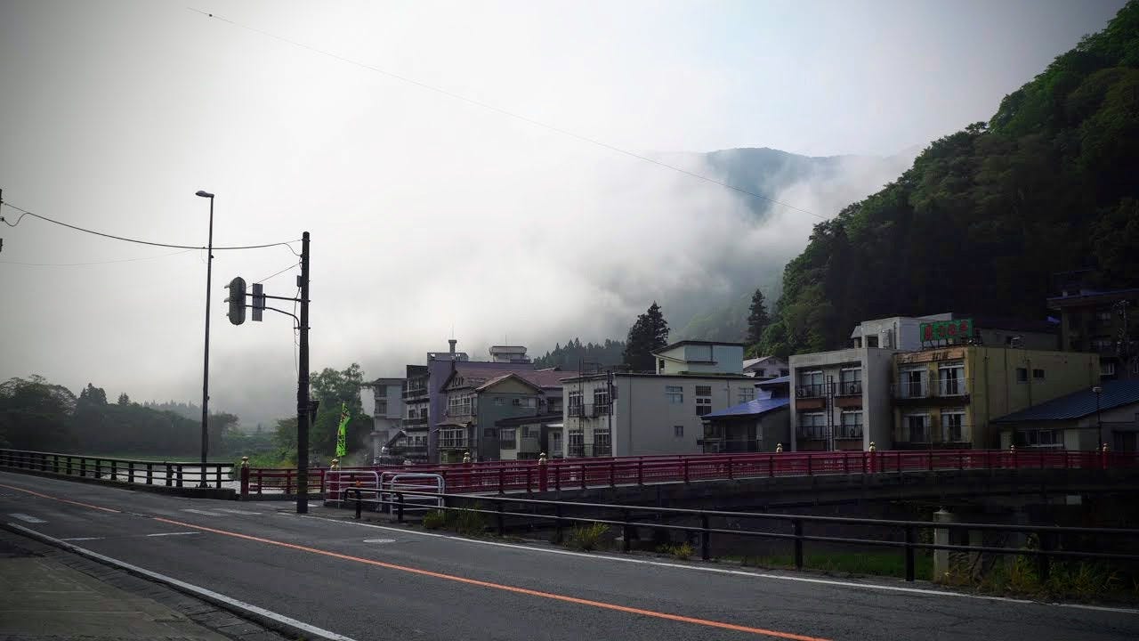 Buildings line along the banks of the Oguni River in Semi Onsen with a mountaintop peaking out in the background through thick fog.