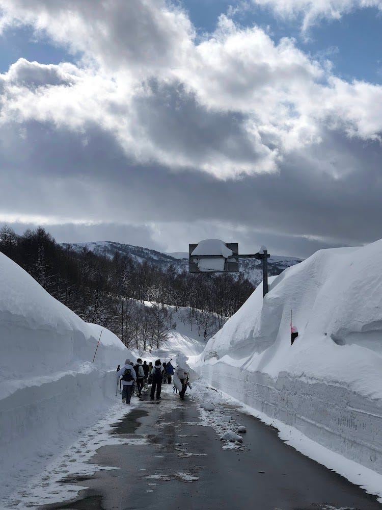 People walking on a road with 5m high banks of snow on the way home from Mt. Yudono Shrine