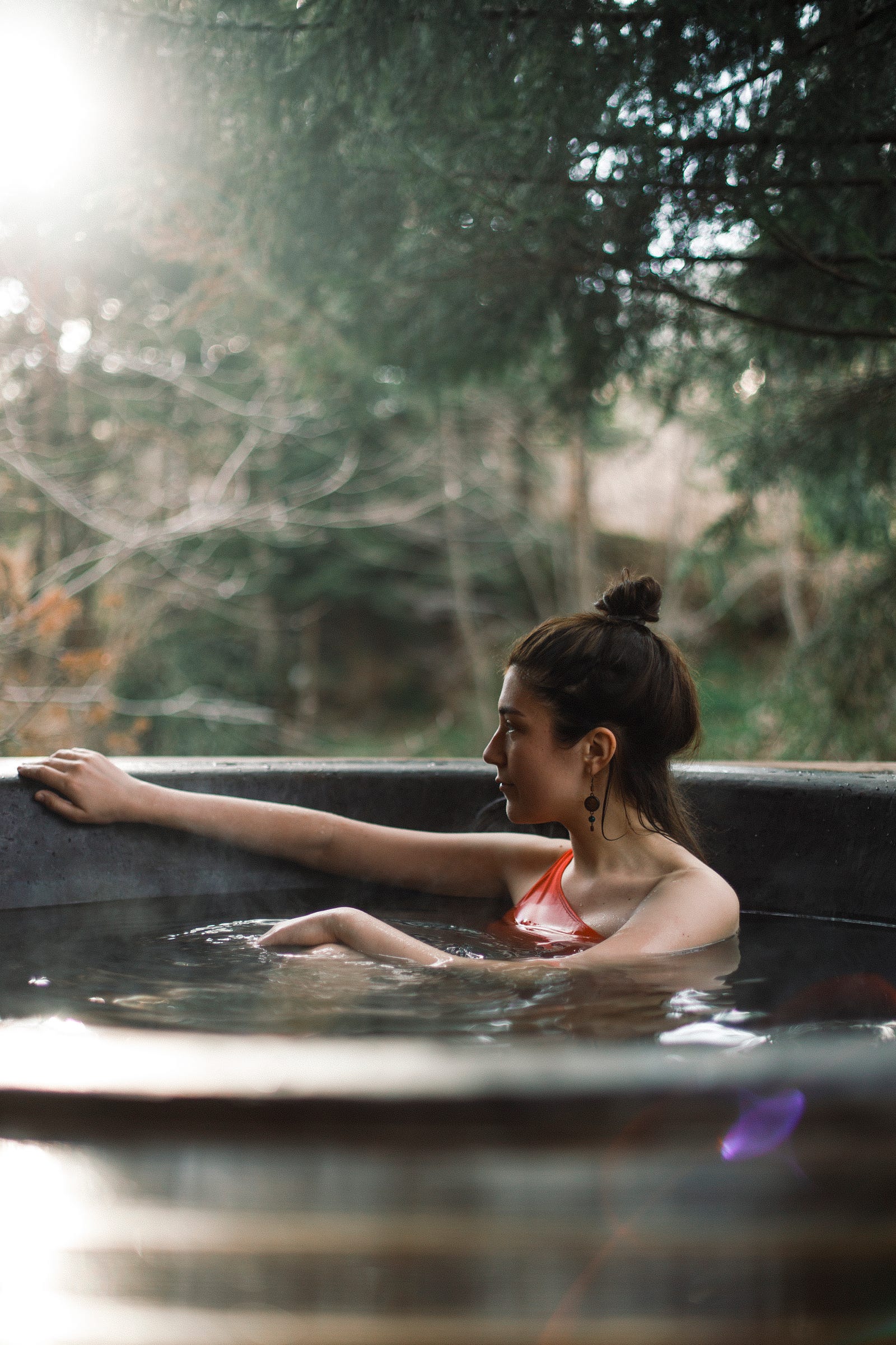 A brunette woman sits in a hot tub, facing to the left. Her right arm is extended to touch the edge of the tub. Hot tubs are notorious for harboring various waterborne pathogens, including bacteria, viruses, and fungi. Insufficient chlorine or bromine levels and improper pH balance can promote the growth of these microorganisms, posing a significant health risk to hot tub users.