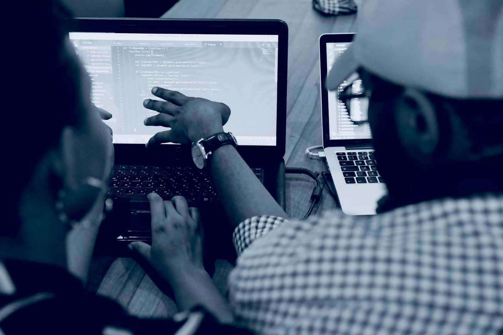 A woman using a laptop computer beside a person wearing a hat