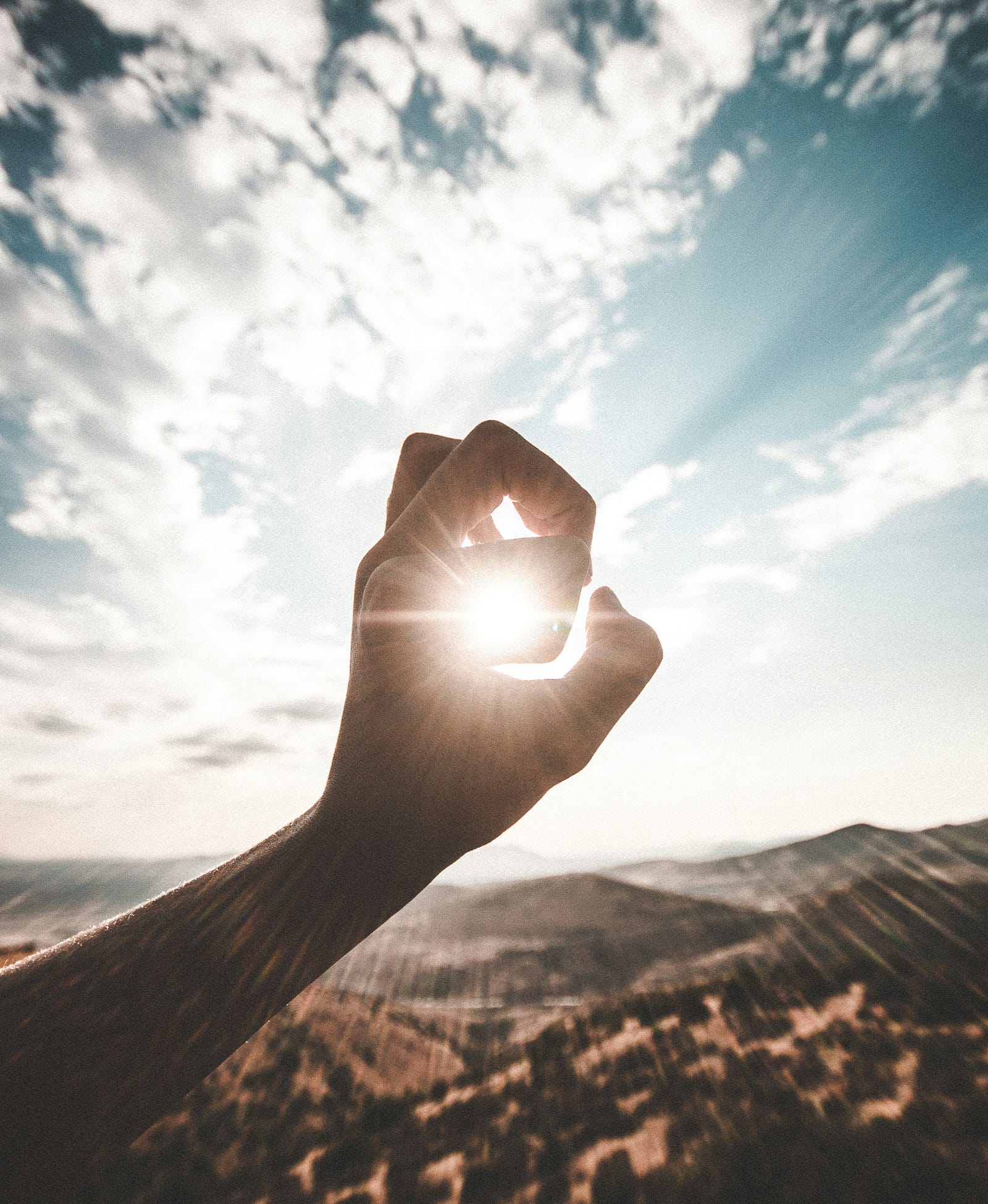 A hand extends up, with fingers formed to wrap around the distant sun.
