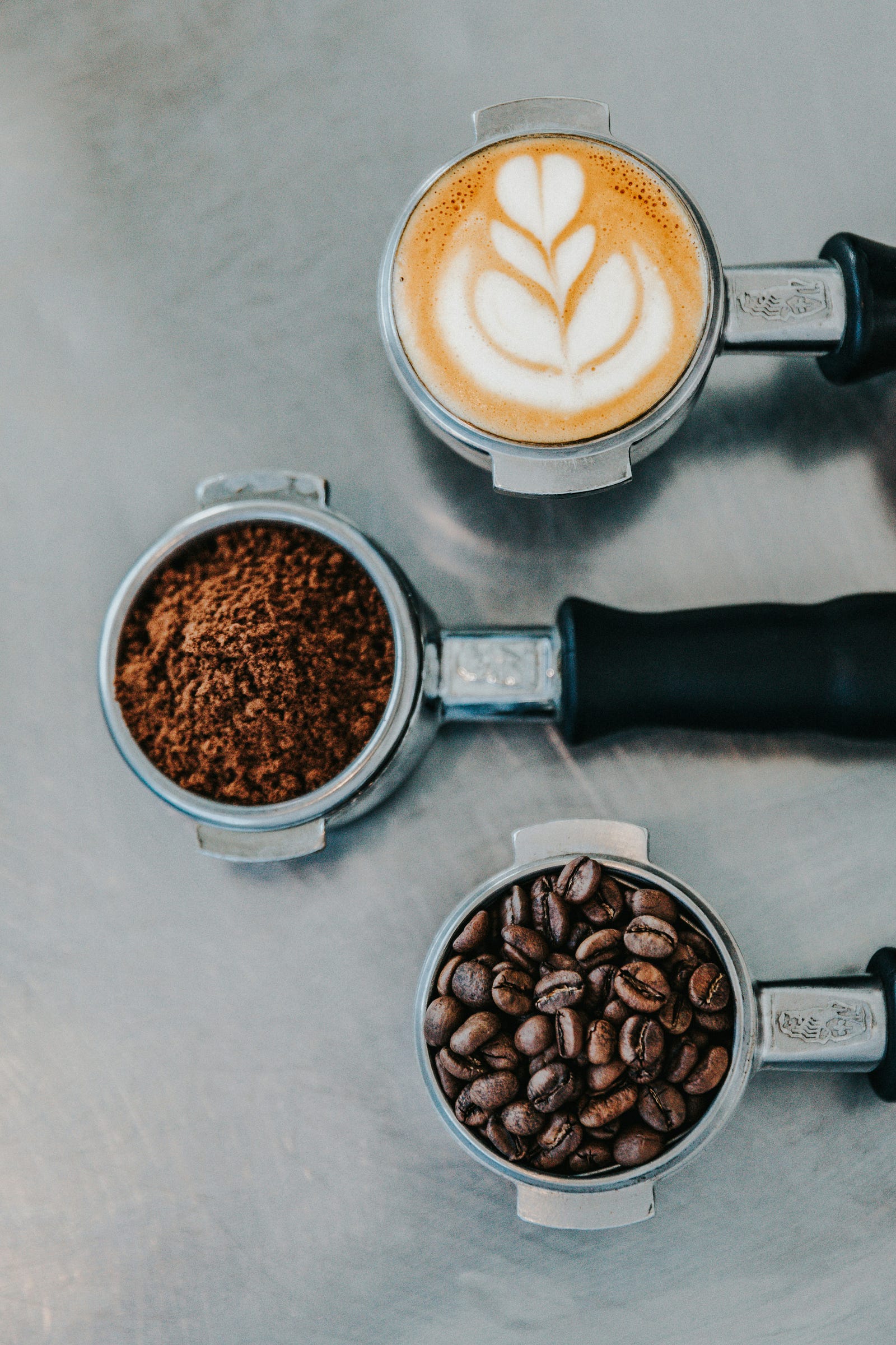 Three small round devices (with handles) each hold various coffee types, ready to be placed in a machine and grinded.