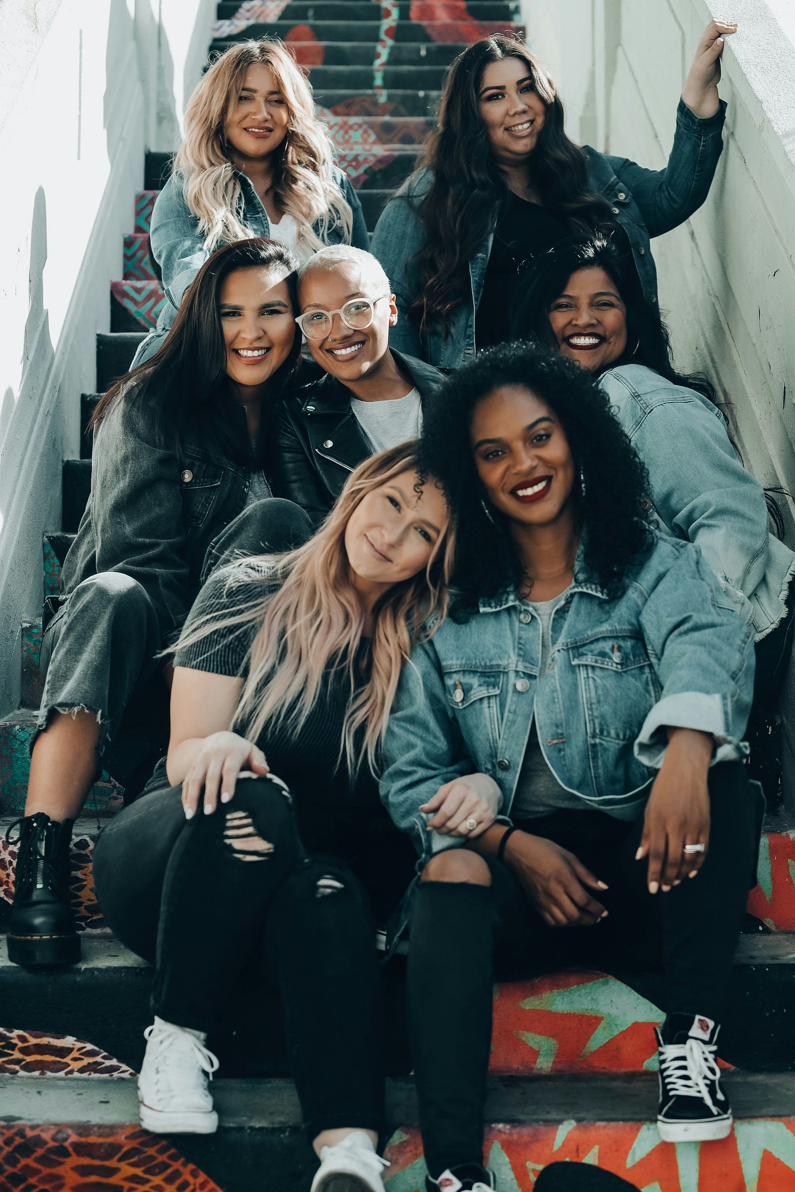 A group of youngish women, of various races, sit on a staircase.