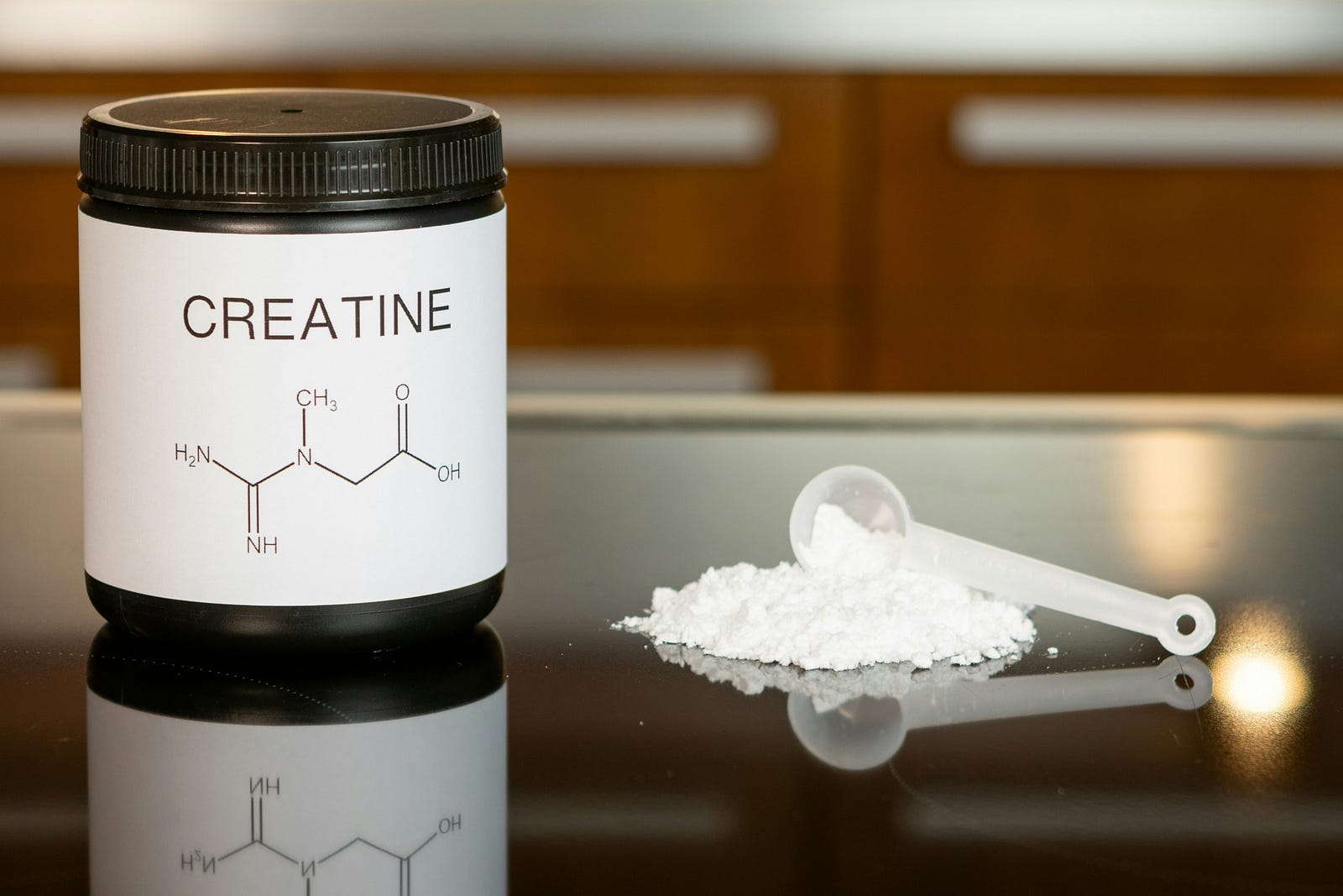 A bottle of creatine on the left, with white powder and a small spoon on the right.