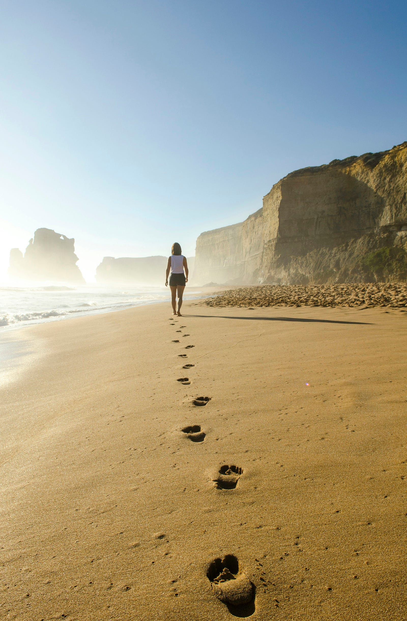 A woman walks away from us on a sandy beach.