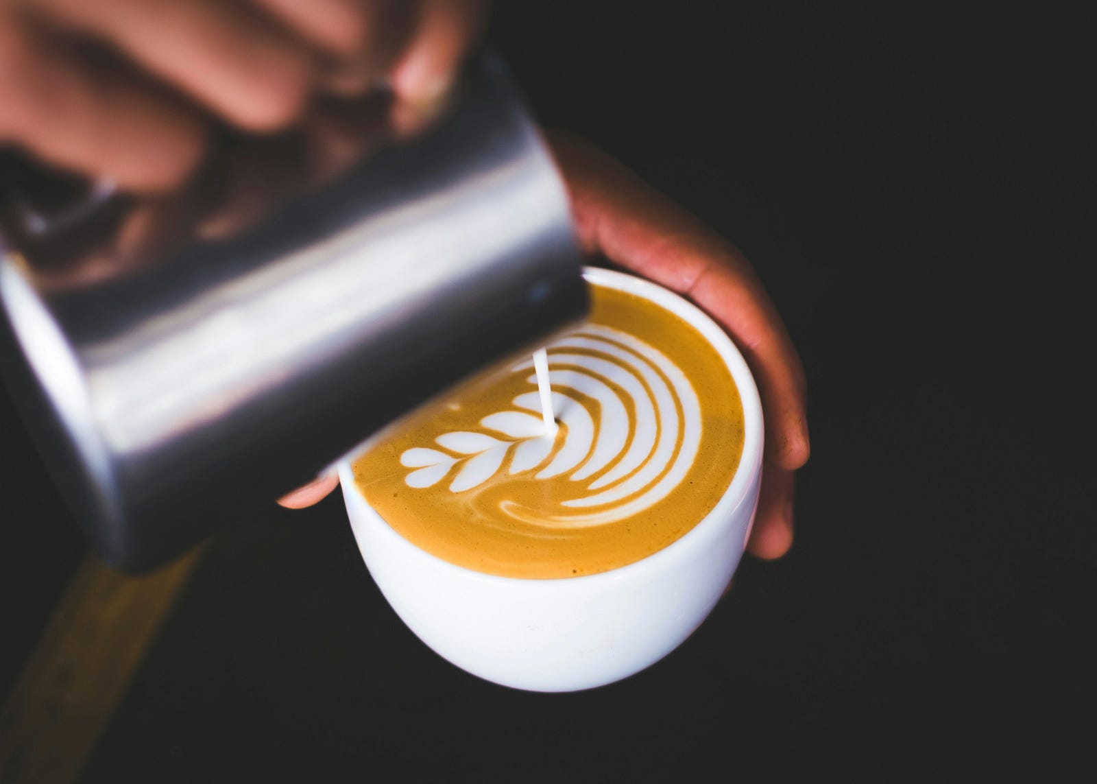 A person pours milk to create a beautiful design for a caffe latte.