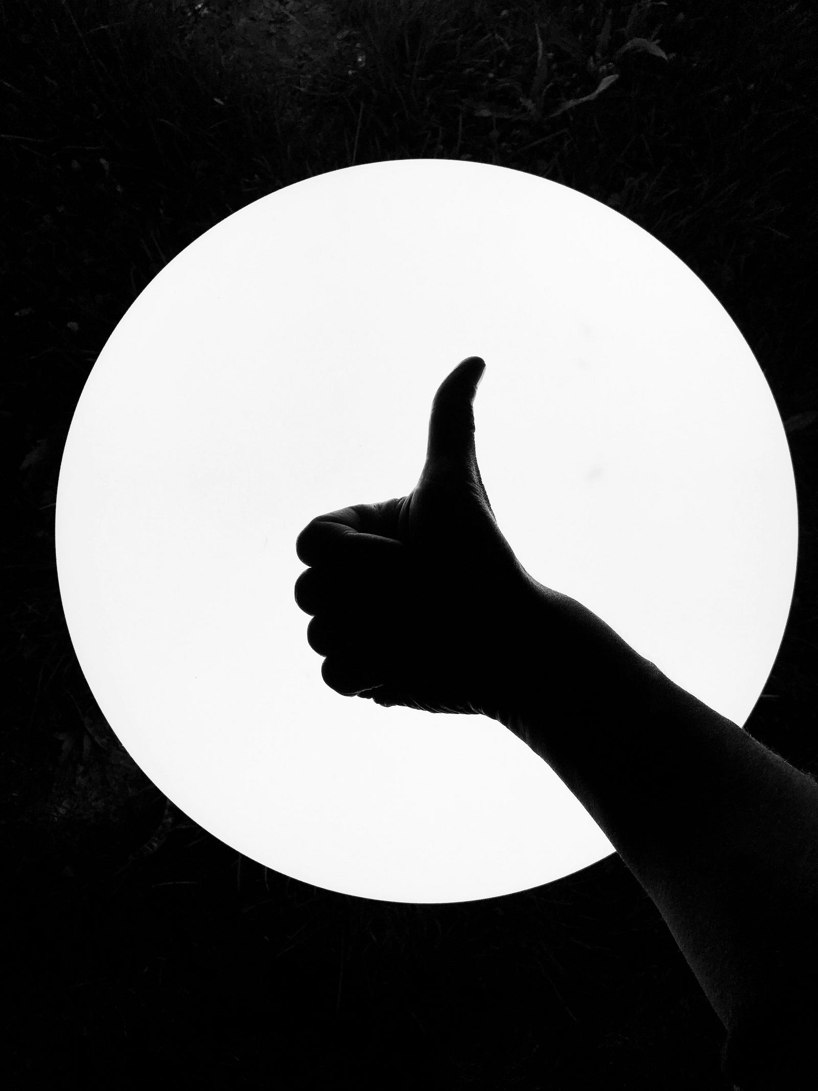 A black and white image of a person offering a thumb’s up gesture.