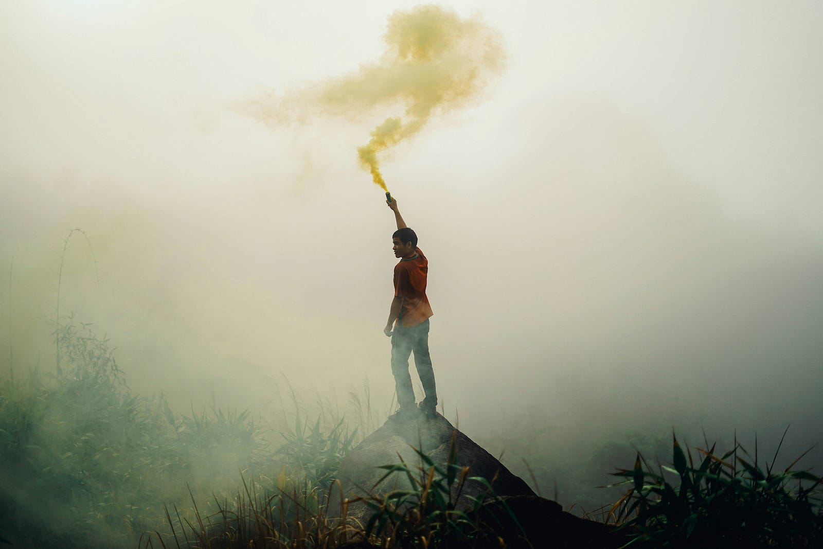 A person on a mountain extends their arm to show a stick with white smoke.