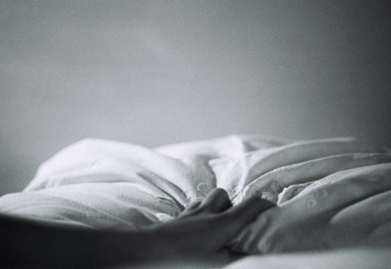 A hand reaches for bedsheets in this black and white image. We only see her arm and hand. Lifestyle factors, such as alcohol consumption and tobacco use, can also affect esophageal health and sleep habits.