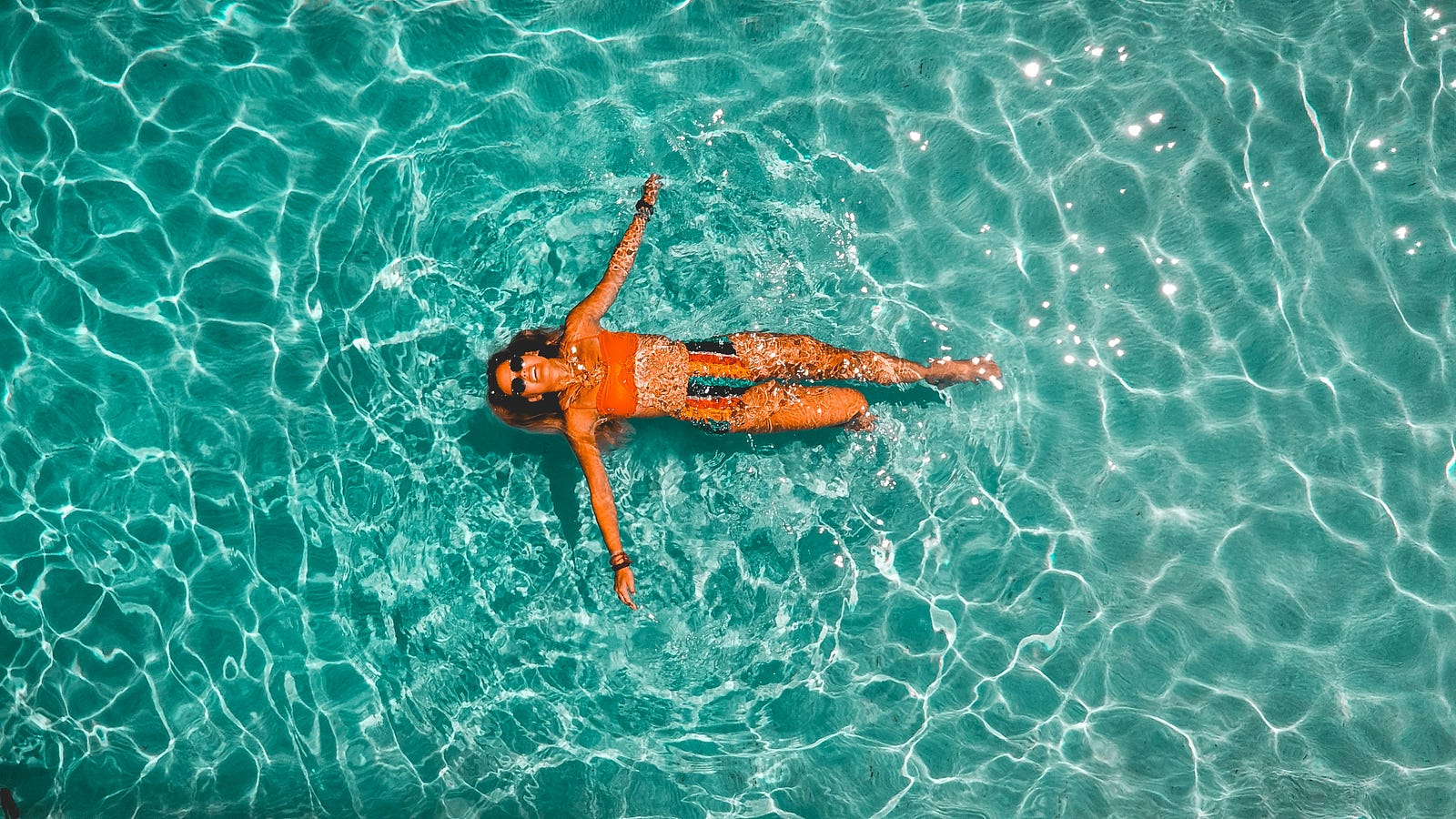 A woman swims on her back in a swimming pool, as seen from above.