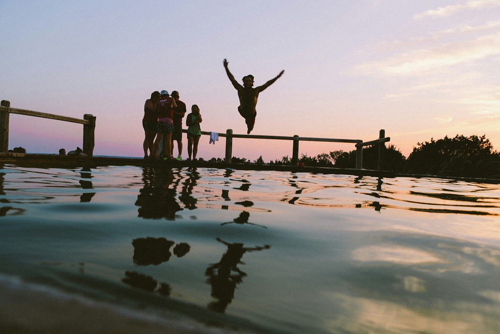 Young people jump into a lake at dusk.