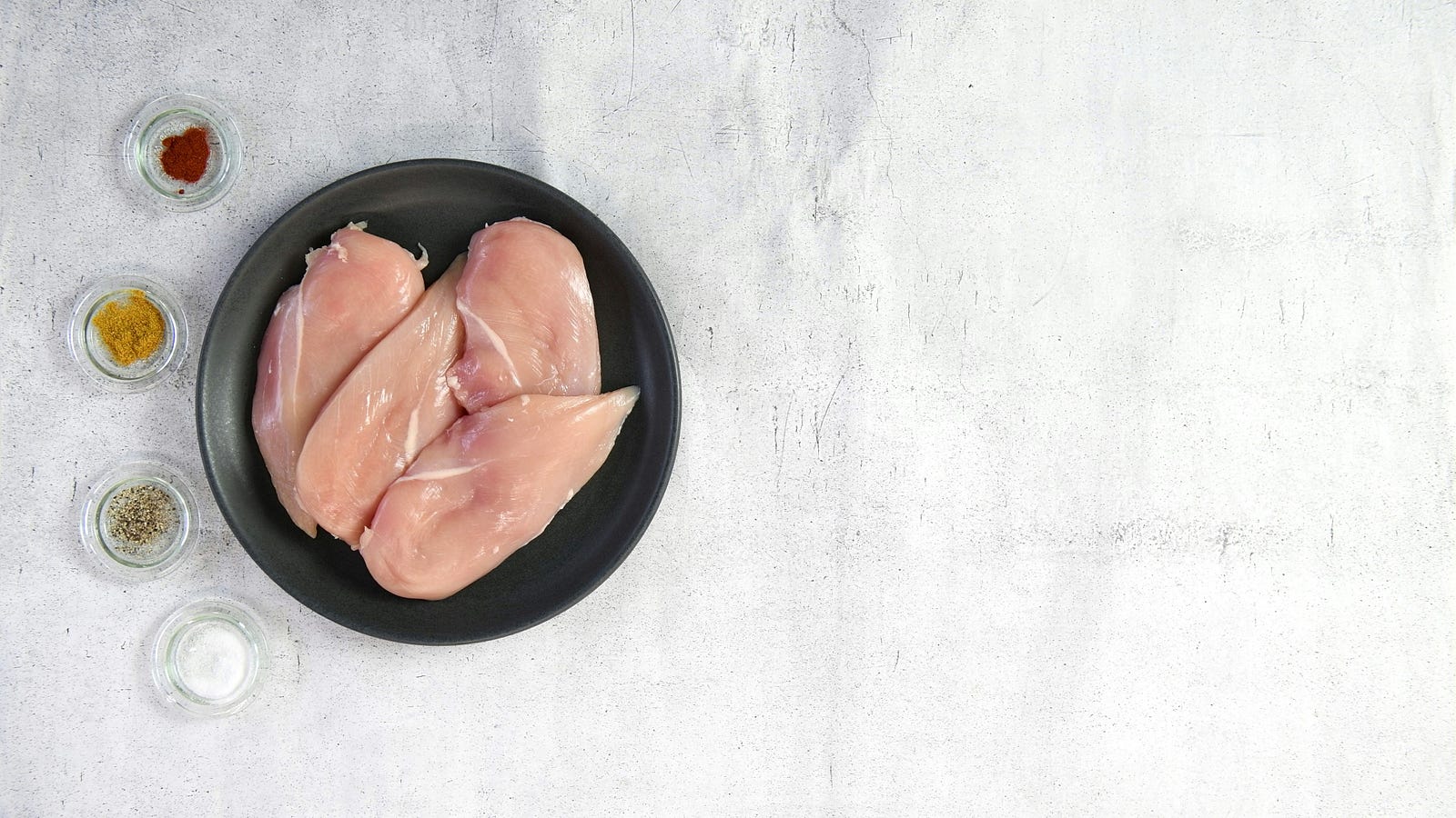 Raw chicken on a black plate.
