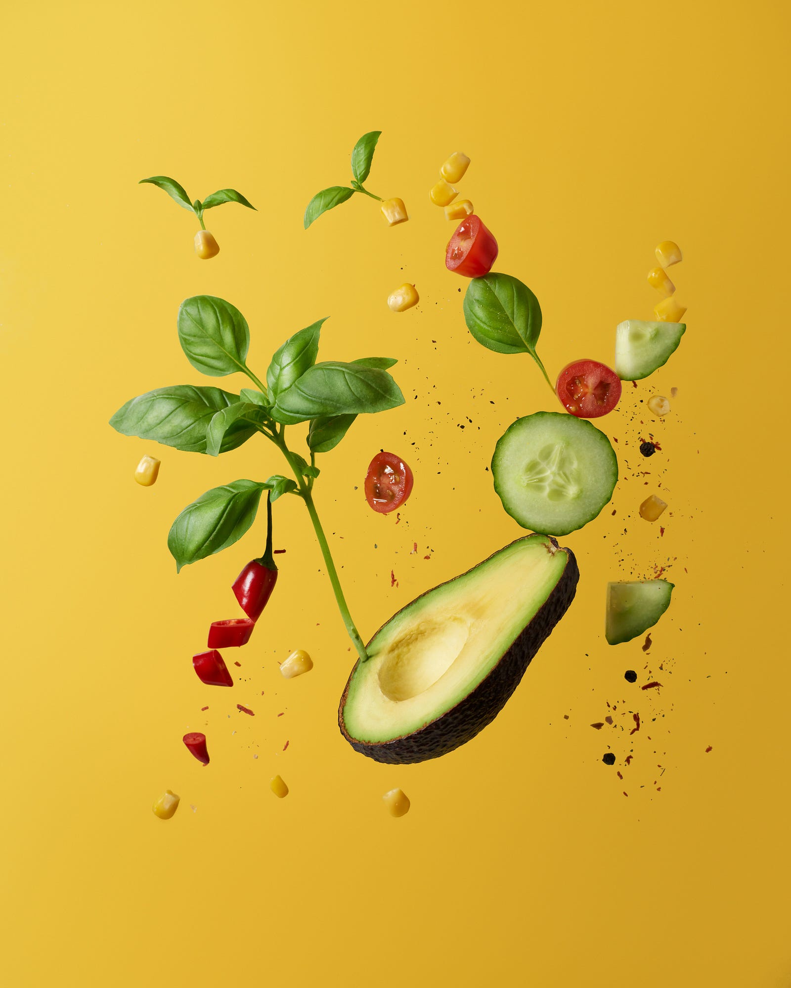 Avocado slices, corn, cucumber slices, and tomato pieces fly into the air.