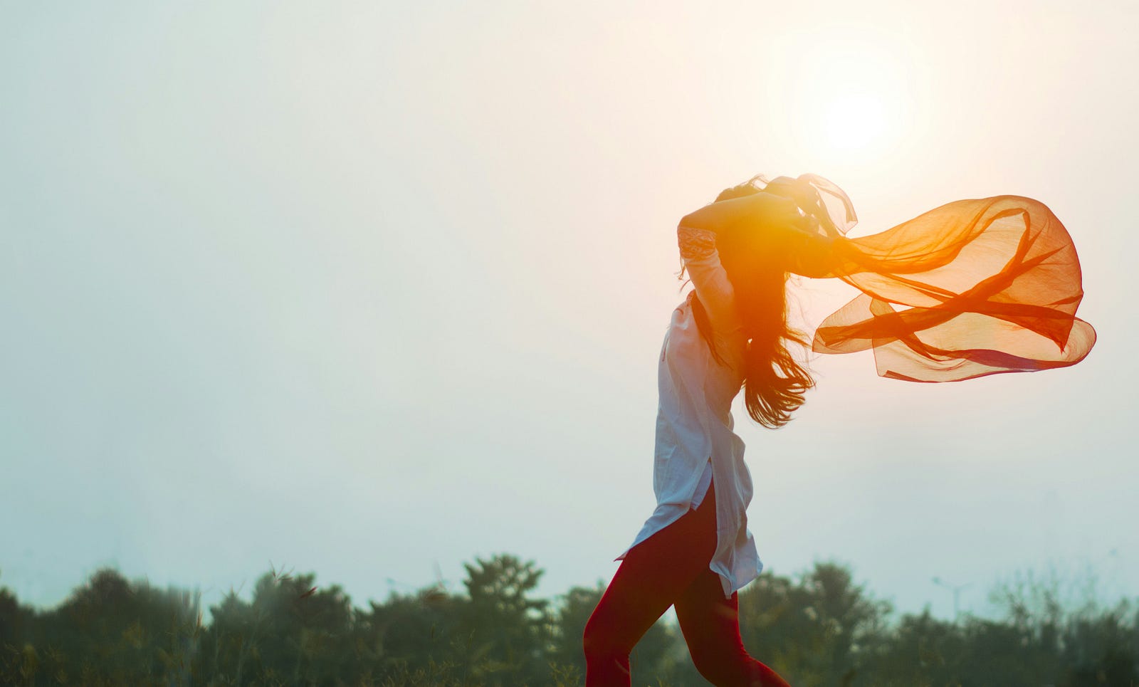 A woman moves from right to left, her orange scarf blown behind her by wind energy.