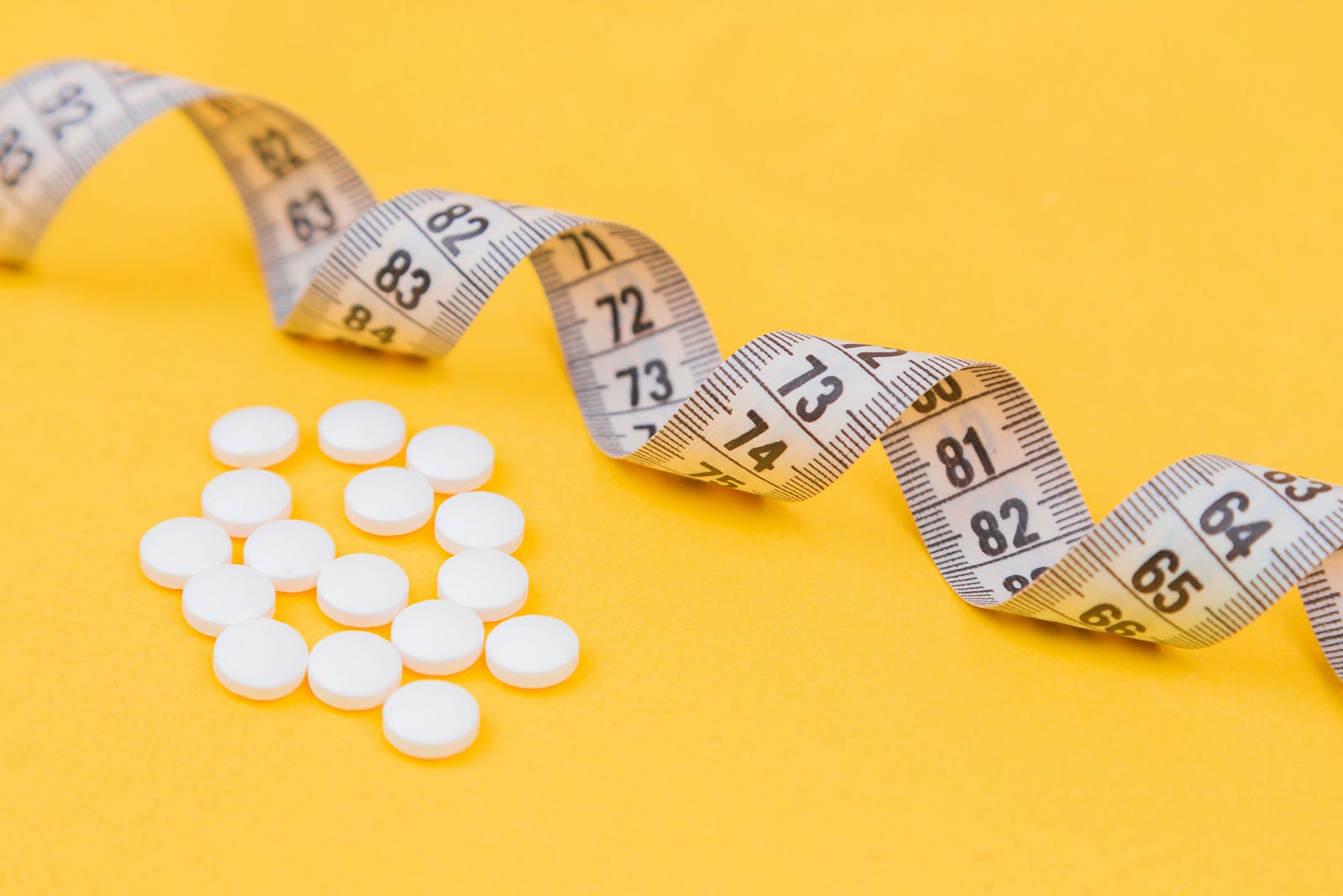 A curling tape measure extends from the upper left to the mid-right. There are a 18 white pills in the lower left quadrant. Mustard-colored background. This essay aims to unravel seven lifestyle recommendations rooted in scientific research, offering practical insights accessible to everyone.