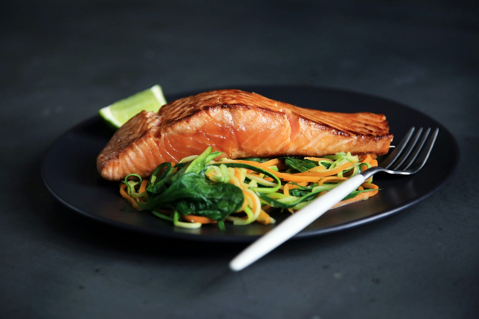 A black plate holds cooked salmon and vegetables.