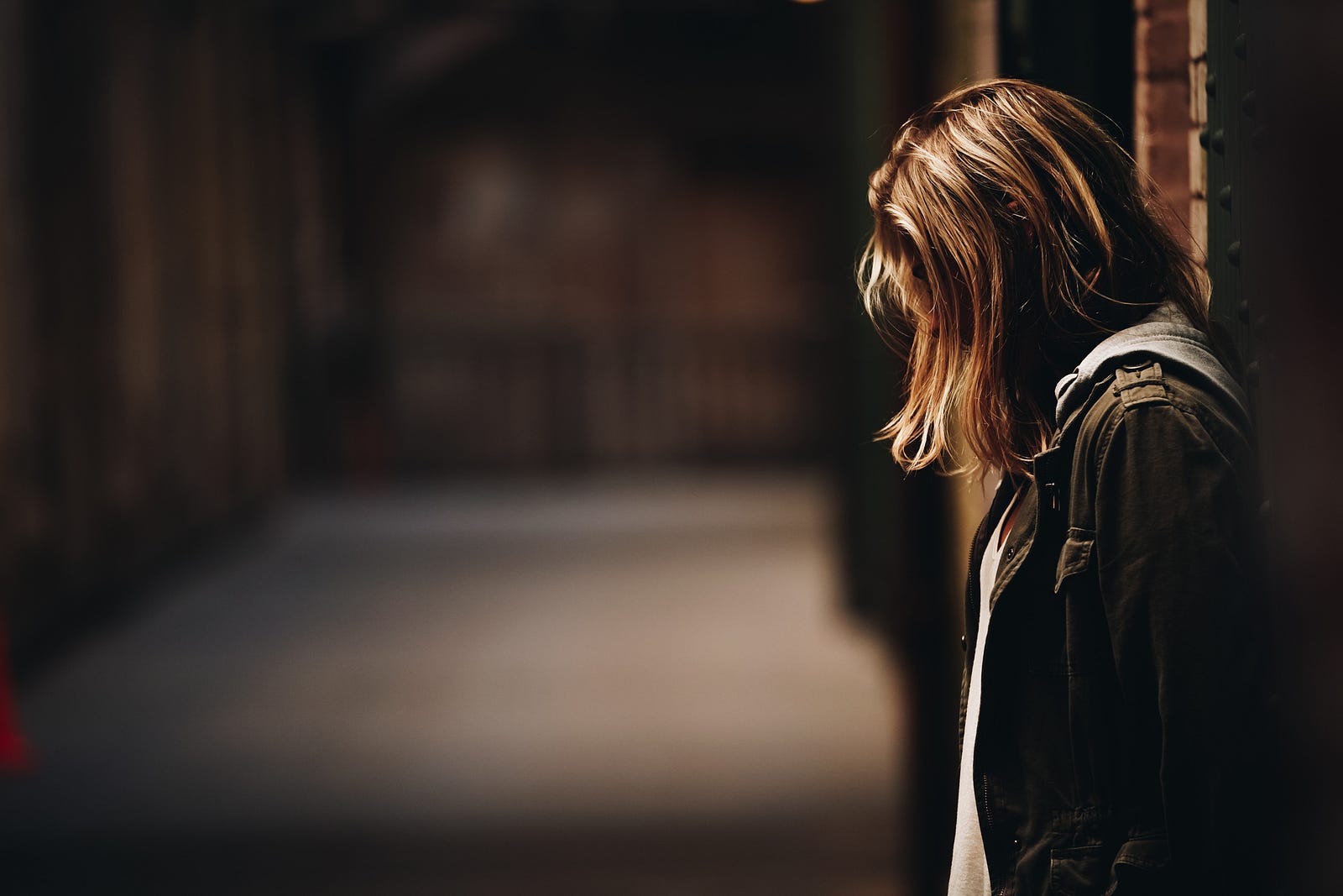 A depressed-appearing young woman has her head facing slightly down as she stands on the right side of an alley. New research suggests that marijuana (cannabis) may improve depression.