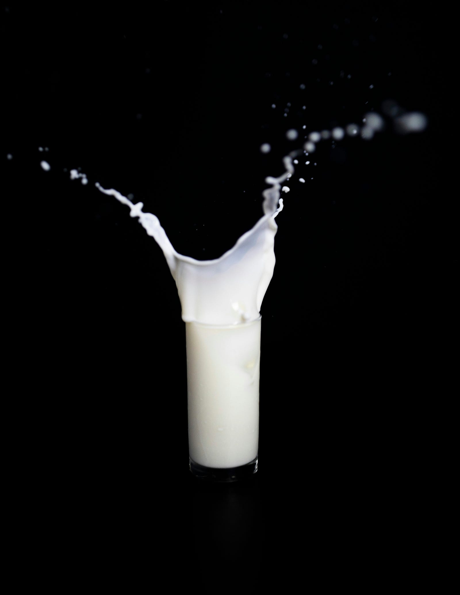 Milk in a tall clear glass spills upwards.
