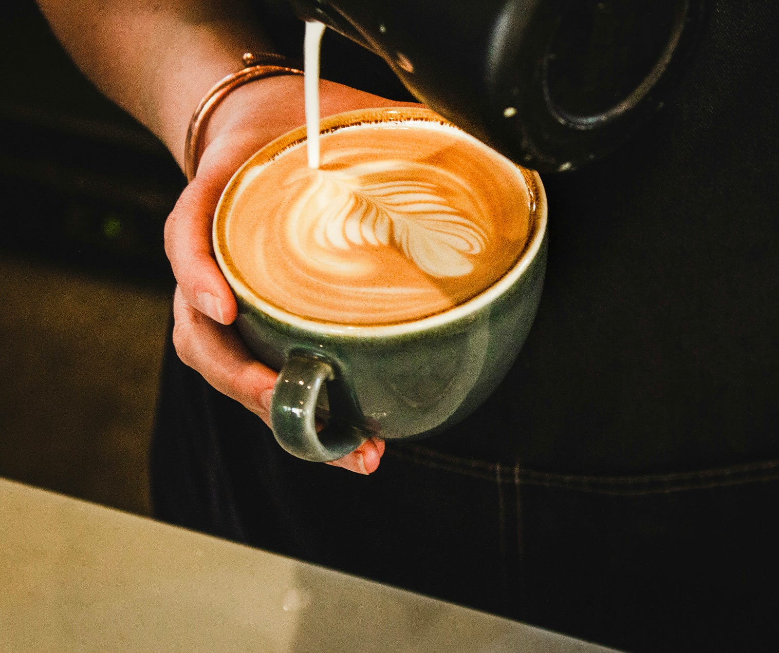 A person pours milk into a cafe latte.