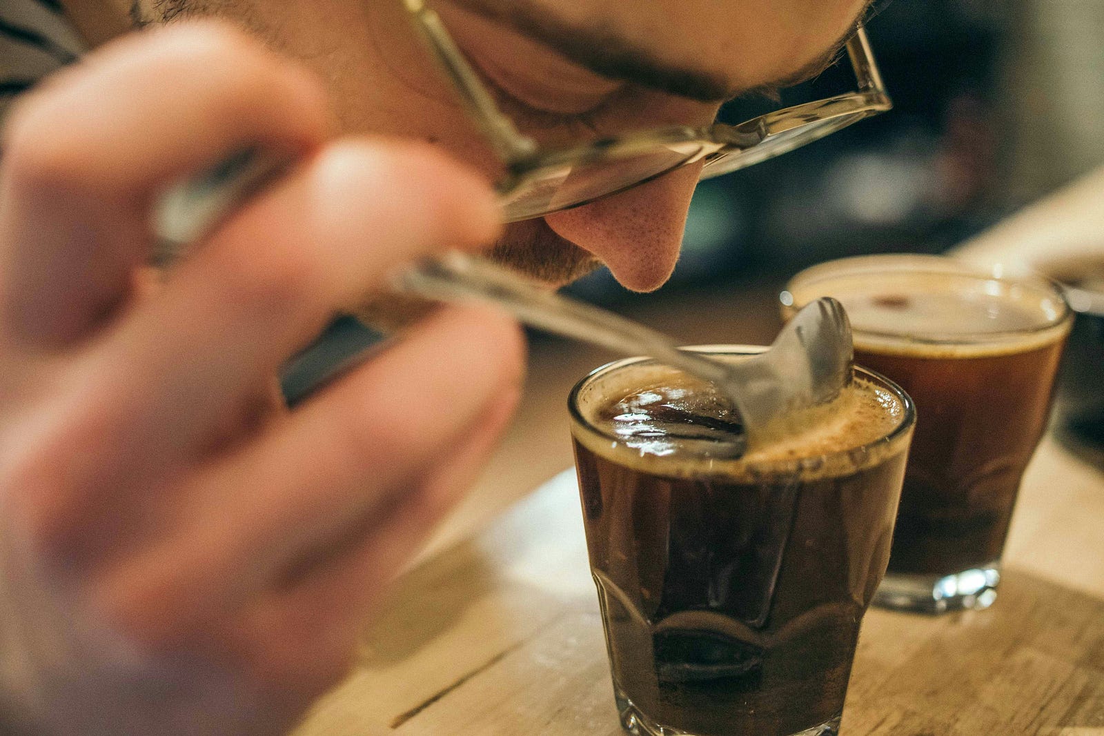 A person brings their nose close to a bevarage in an old-fashioned glass to smell it.