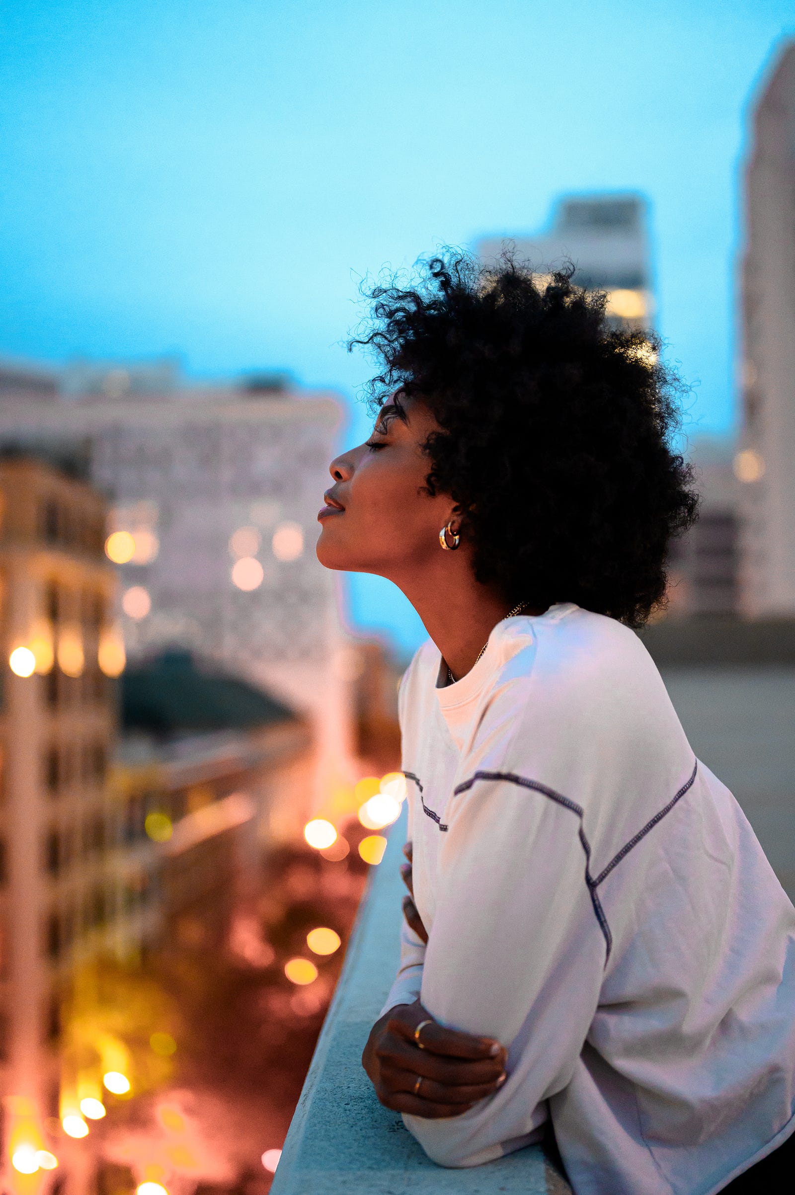 A young black female gazes to the left, the cityscape blurred behind her. Even having one unfavorable social determinant of health doubles an individual’s chances of early death.
