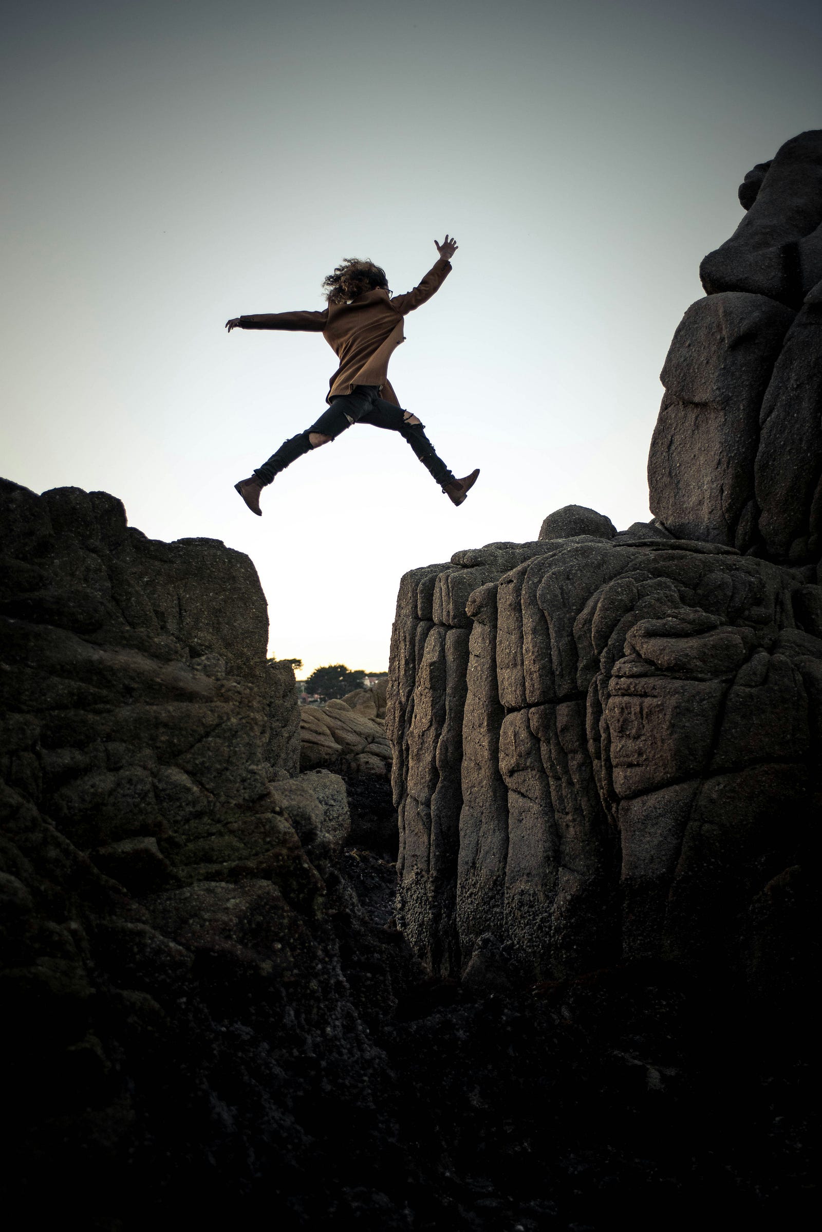 A young person jumps from one moutaintop cliff edge to another.