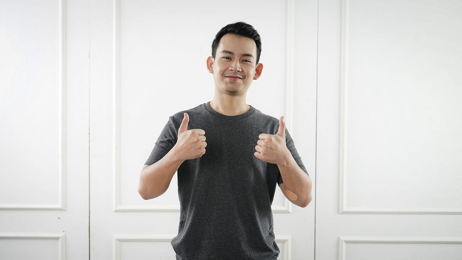 A young Asian man stands with a thumbs-up sign.