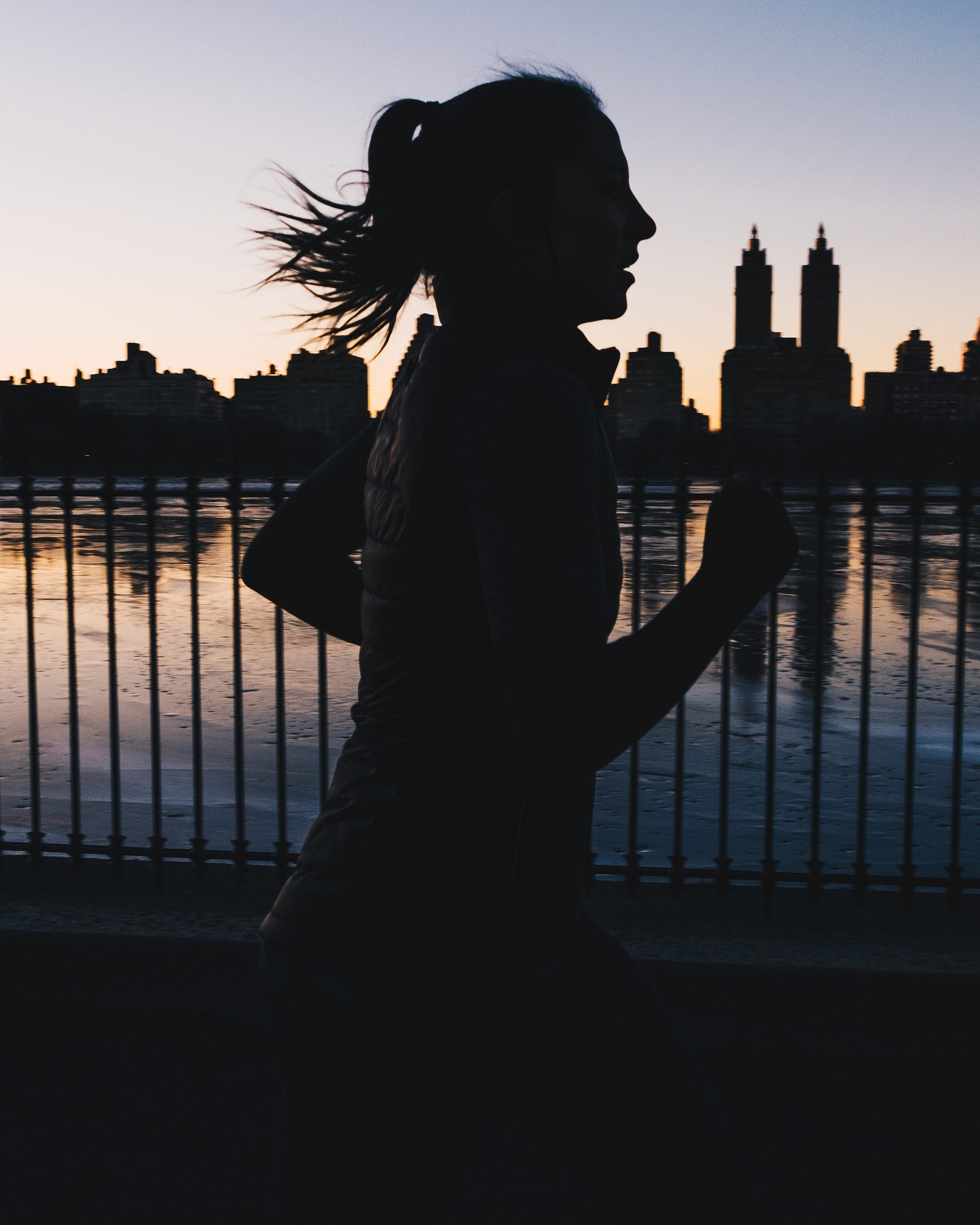 A women runs from left to right, seen in silhouette. There is a lake behind here, with a couple of building spires in the distance. Lifelong endurance exercise is not associated with a better coronary artery calcification profile.