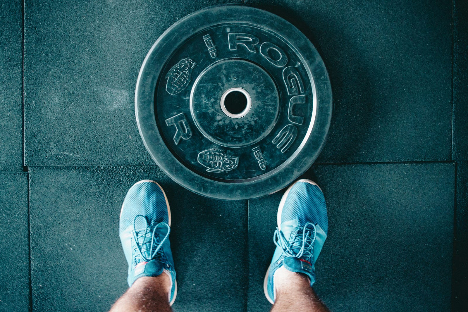 A person stands over a barbell plate. The photo is take from above.