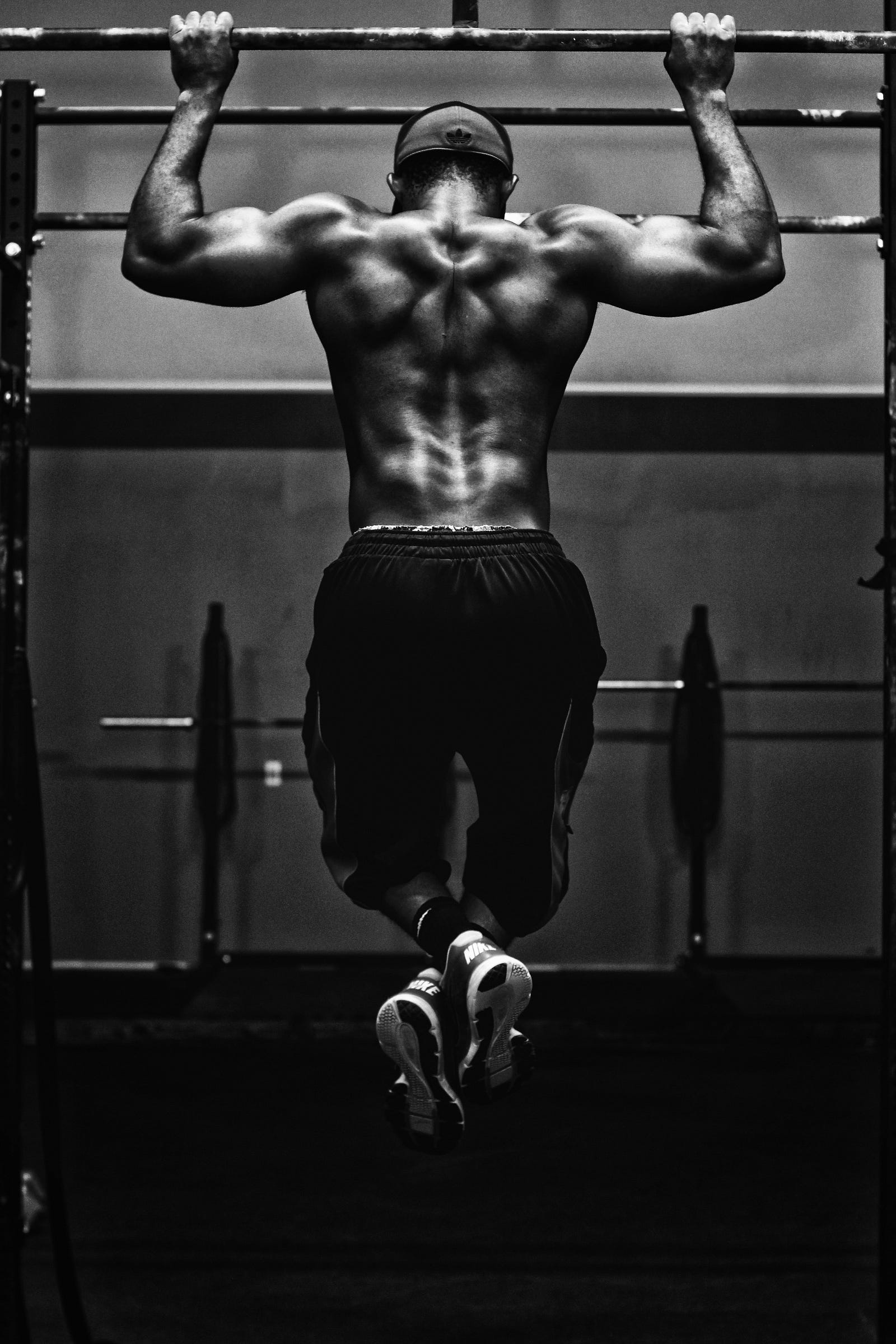 A muscular man does a pullup. We see him from behind in this black and white photo.