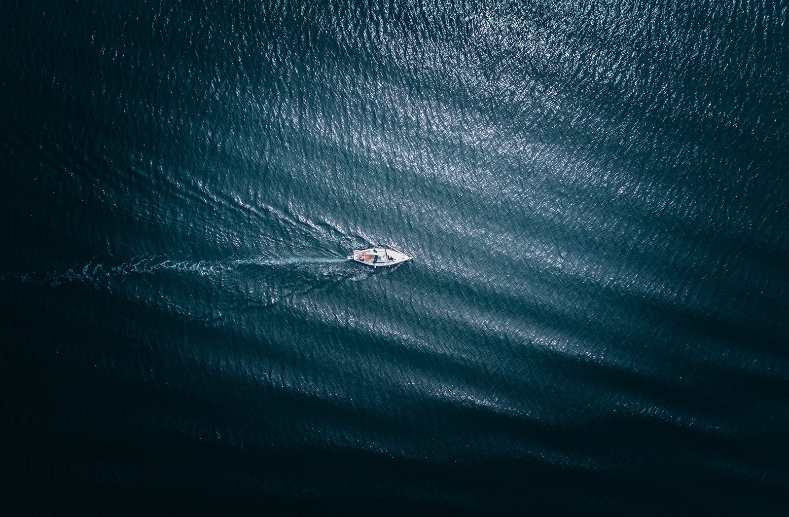 A solo boater is seen from far above in the dark blue sea. When the alternative is not sleeping at all, polyphasic sleep might be helpful. For example, some solo sailors adopt a polyphasic sleep schedule leading into a race to help them manage limited sleep while racing.