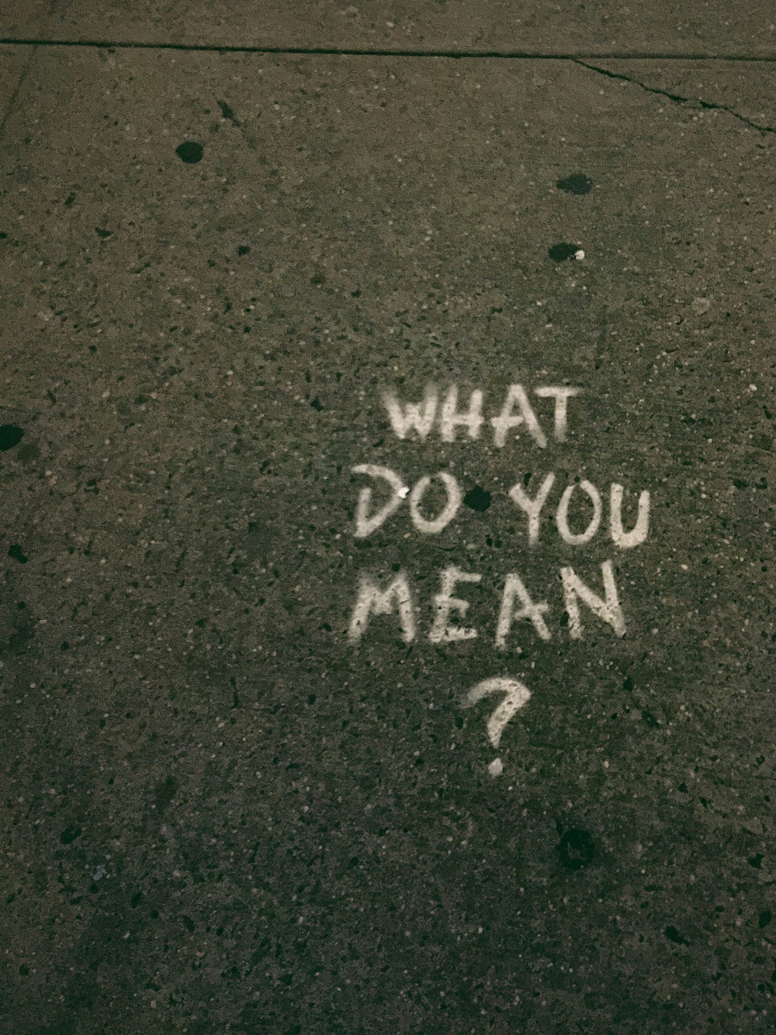 “WHAT DO YOU MEAN?” is written in white letters on pavement.