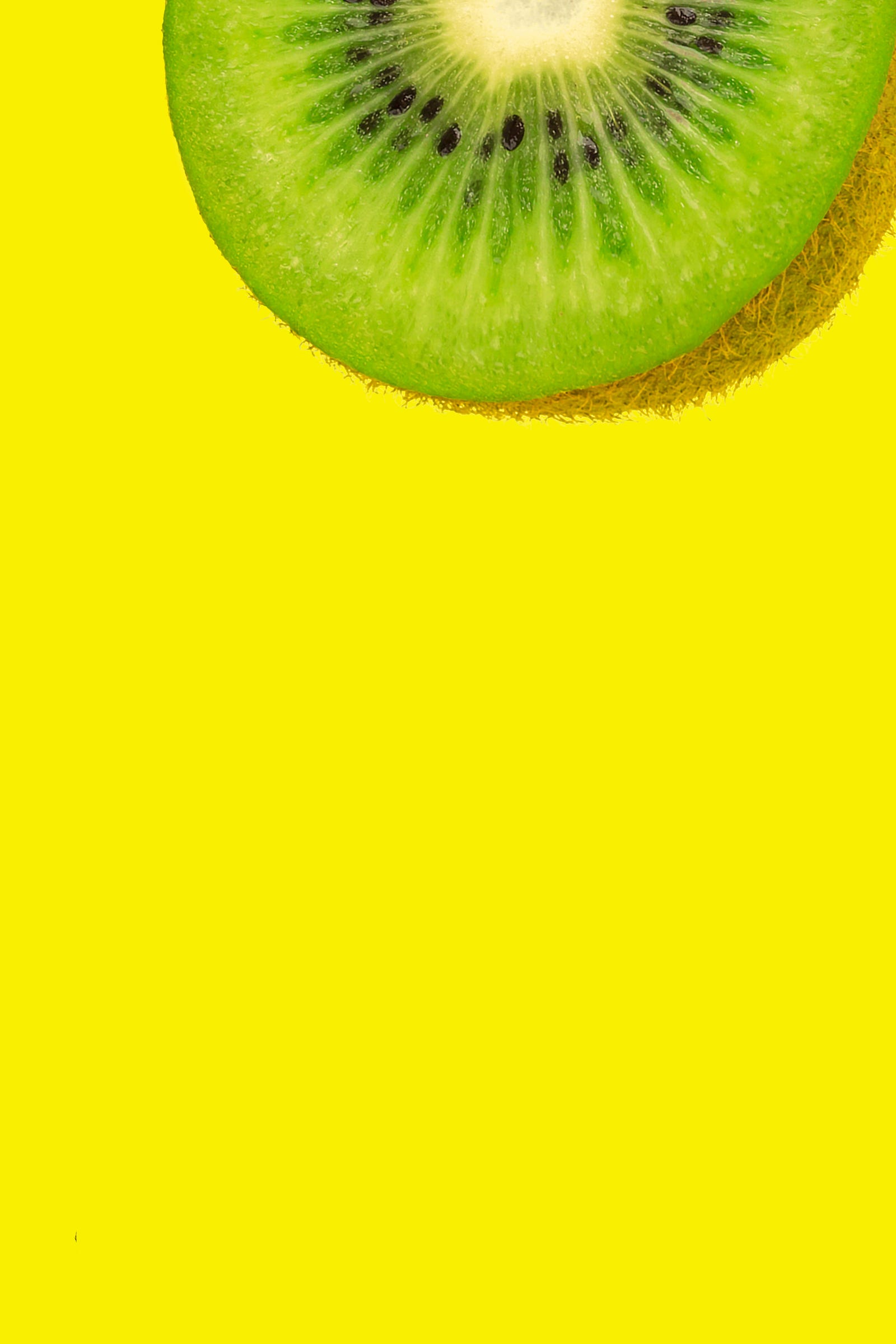 We see half of a slice of kiwi fruit emerging from the image top. Bright yellow background.