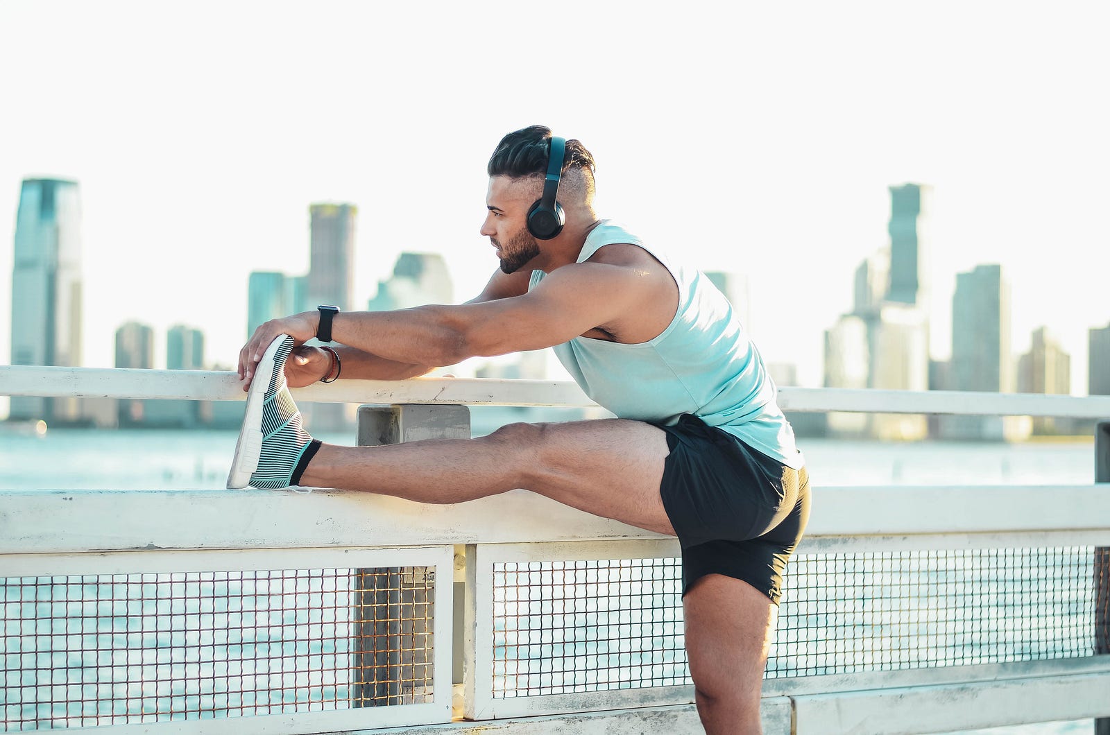 A man lifts his leftc leg to the top of a fence to stretch. Static stretches before exercise can be detrimental to performance, while dynamic stretching may have value.