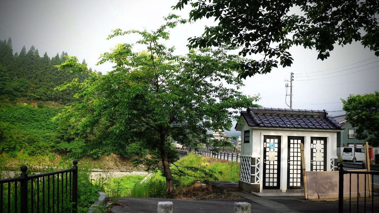 A tree and small building in Japanese livery alongside the Oguni River in Semi Onsen
